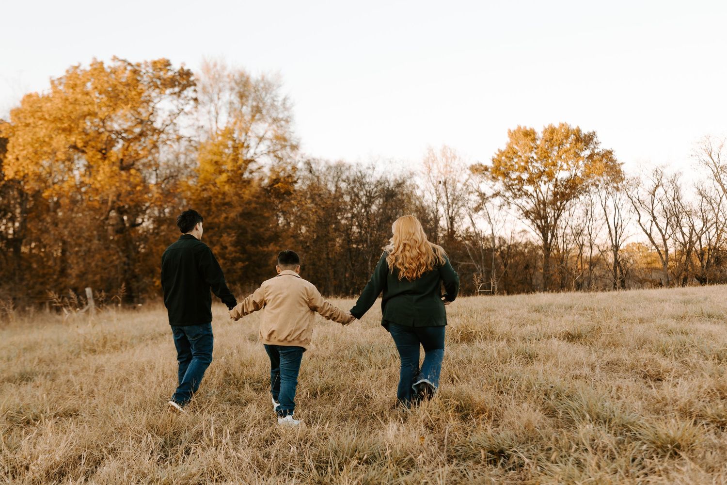 Family walking hand in hand through a golden autumn field at sunset.