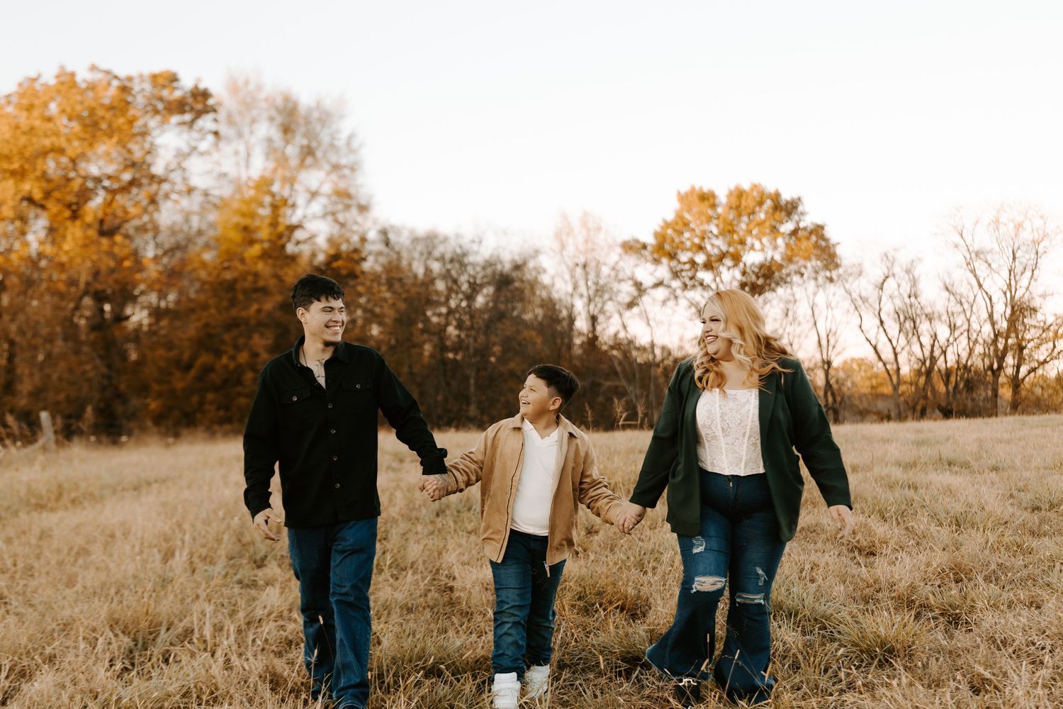 Family of three walking together through a fall meadow with warm lighting.
