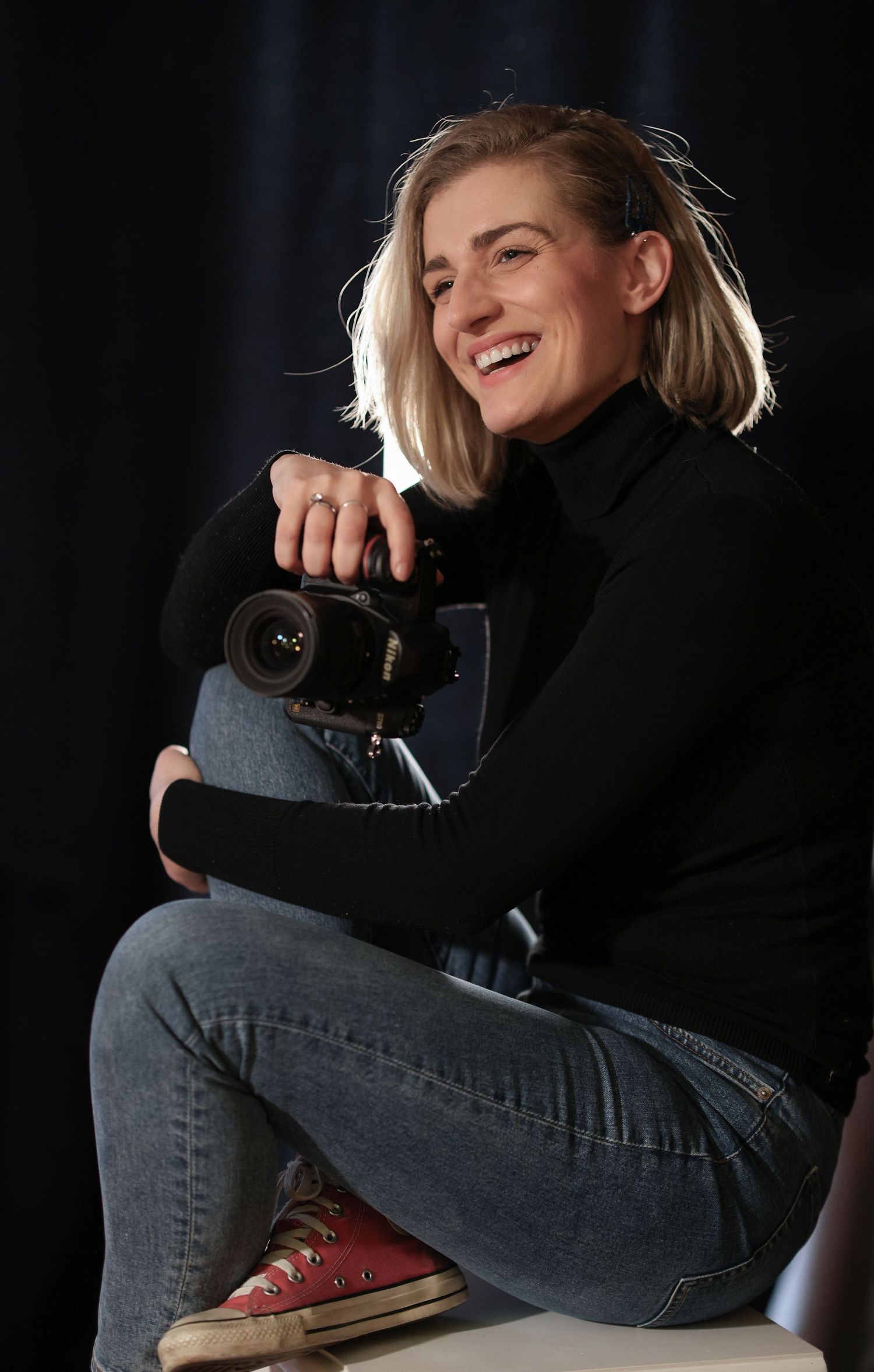 Irish photographer holding her camera and laughing while having her photos taken in studio