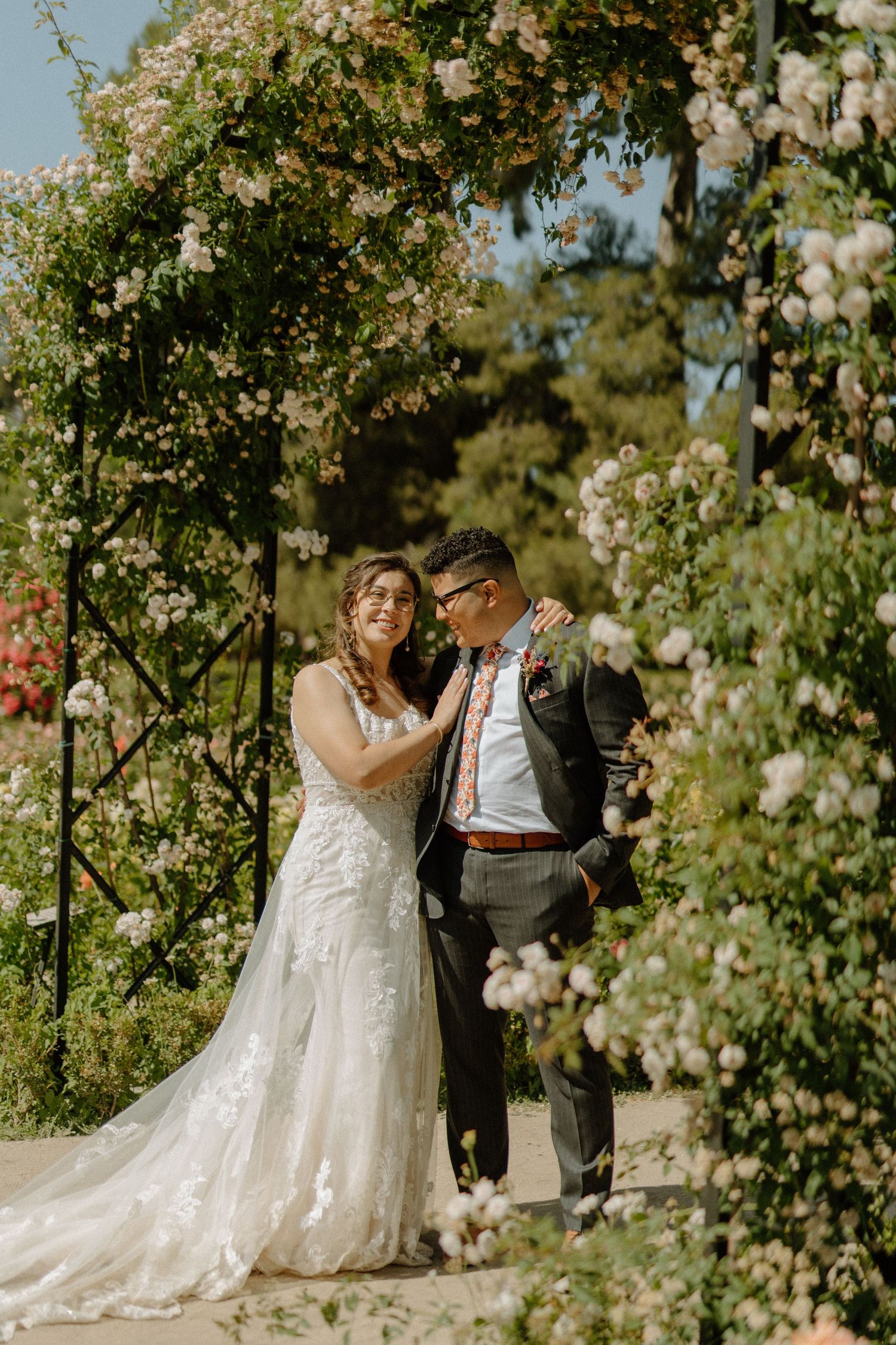 A couple shares an intimate moment under a romantic floral arch in a garden wedding setting.
