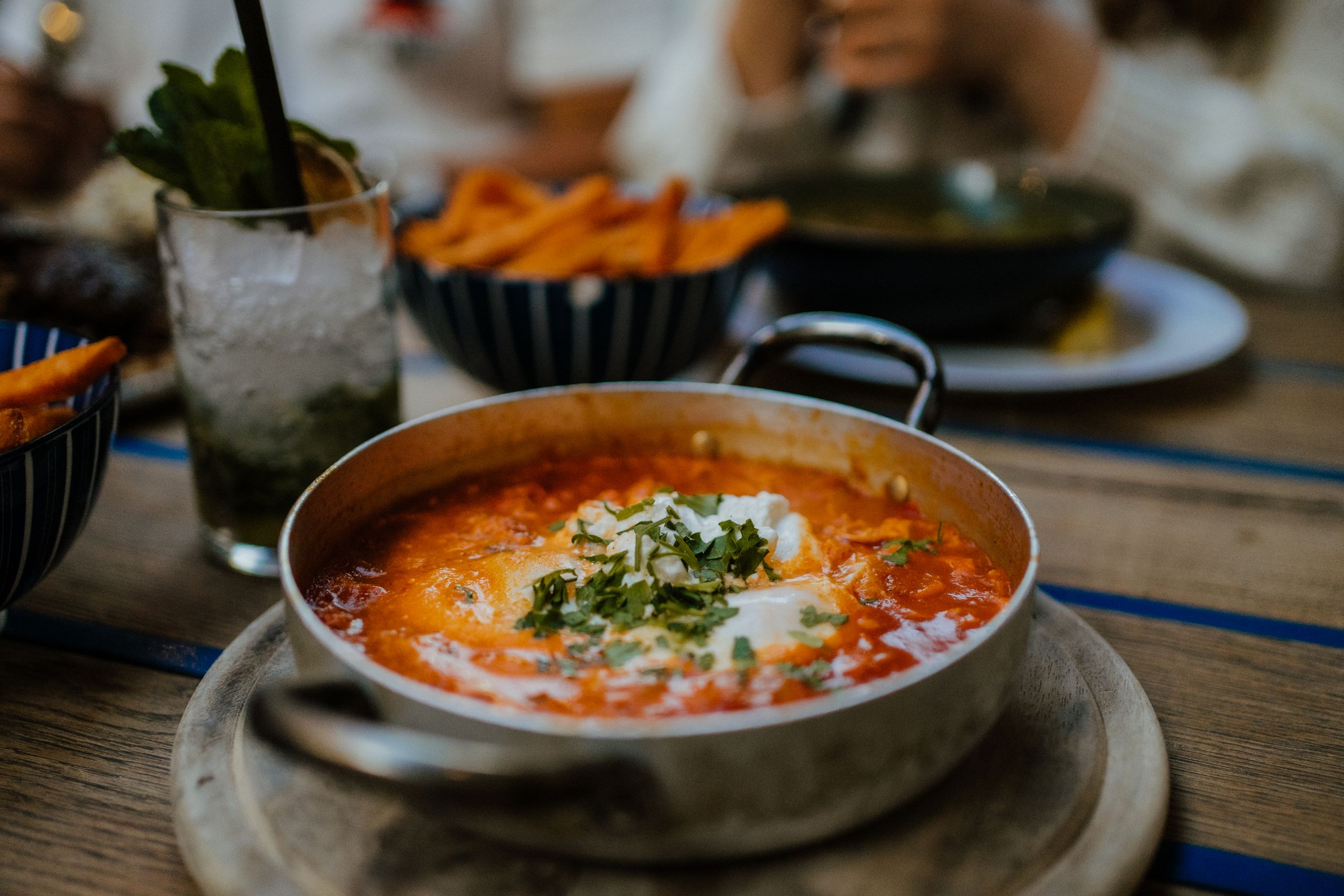 A bowl of creamy tomato soup garnished with fresh herbs and cream served in a rustic ceramic bowl on wooden table.