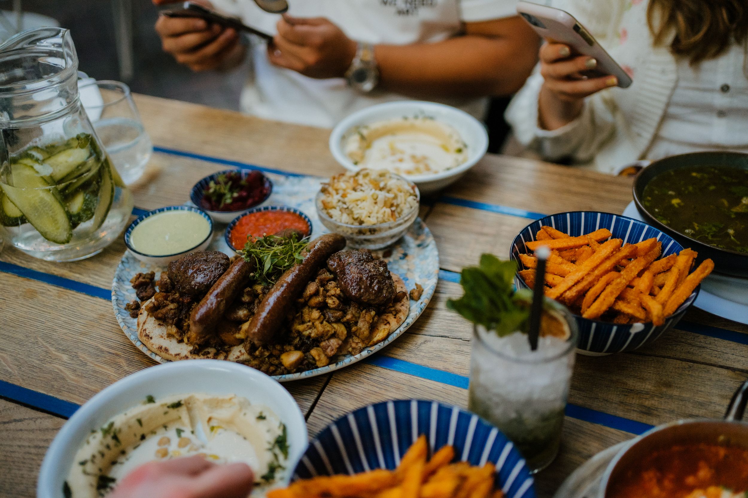 A spread of Asian-inspired dishes on blue plates including marinated meats, carrots, and various sides on a wooden table.