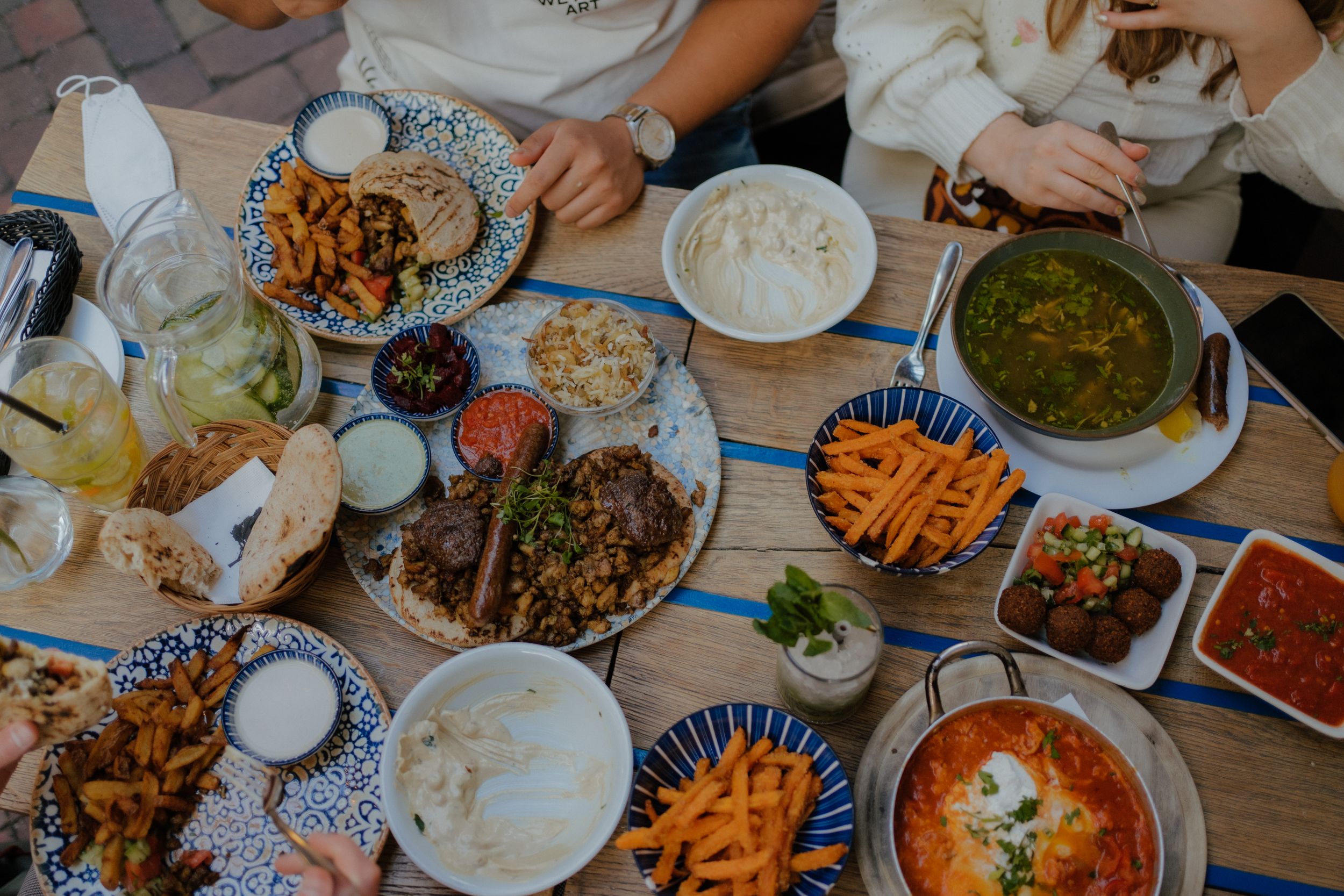 A spread of Asian dishes on a wooden table including soups, noodles, carrots, and various side dishes in small plates.