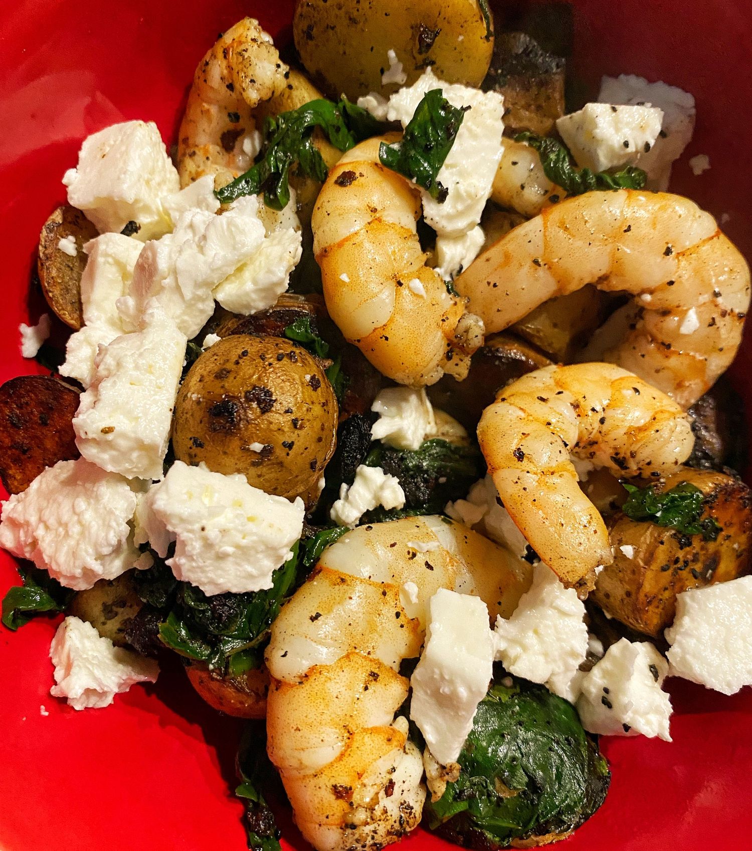 Sautéed shrimp and crumbled feta cheese garnished with fresh herbs on a bright red plate.