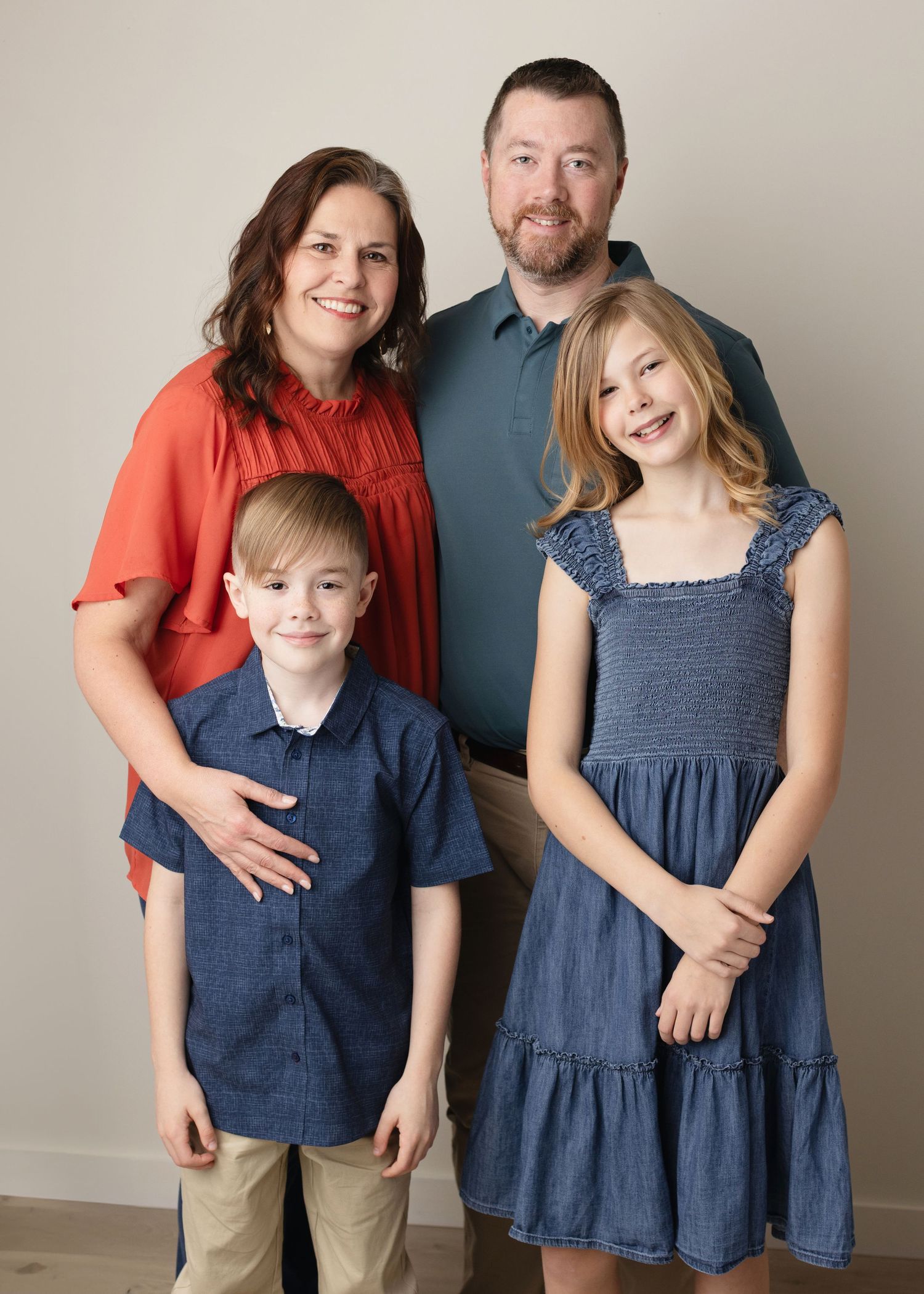 A family of four poses for a portrait wearing coordinating navy blue and coral outfits against a neutral background. Elizabeth Lang Photogra