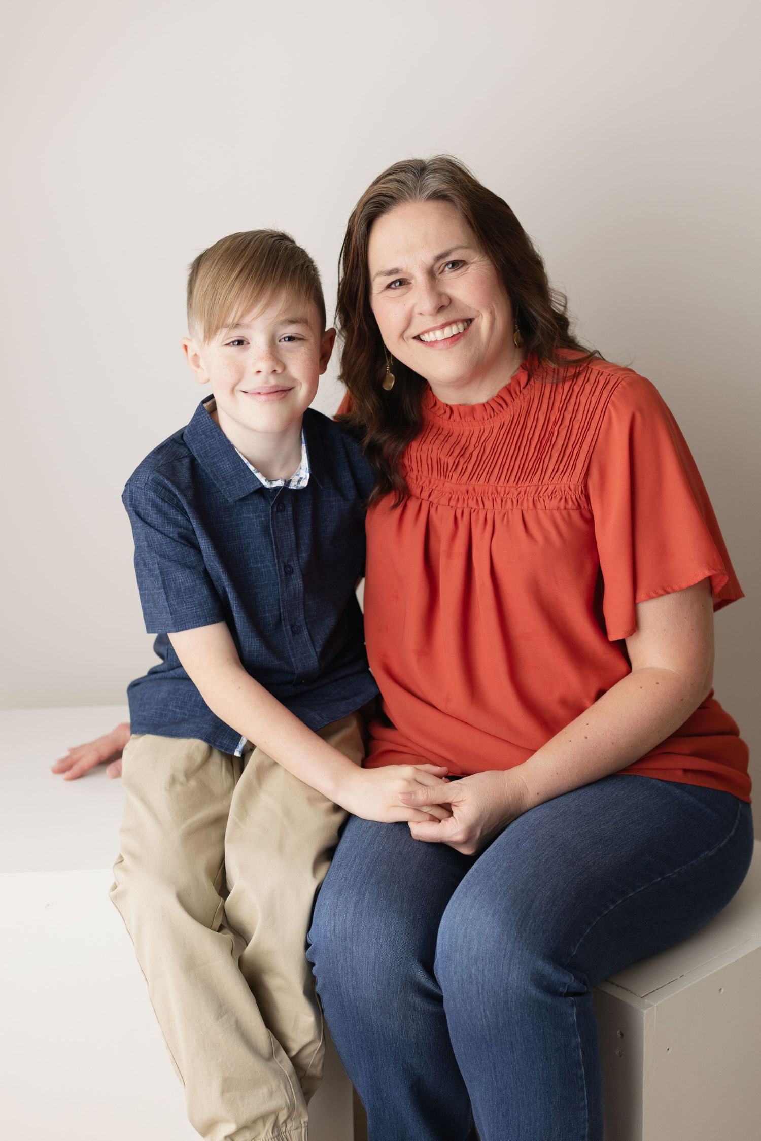 A pair in coordinating outfits of rust orange and navy blue pose together on a light background. Elizabeth Lang Photography Surrey