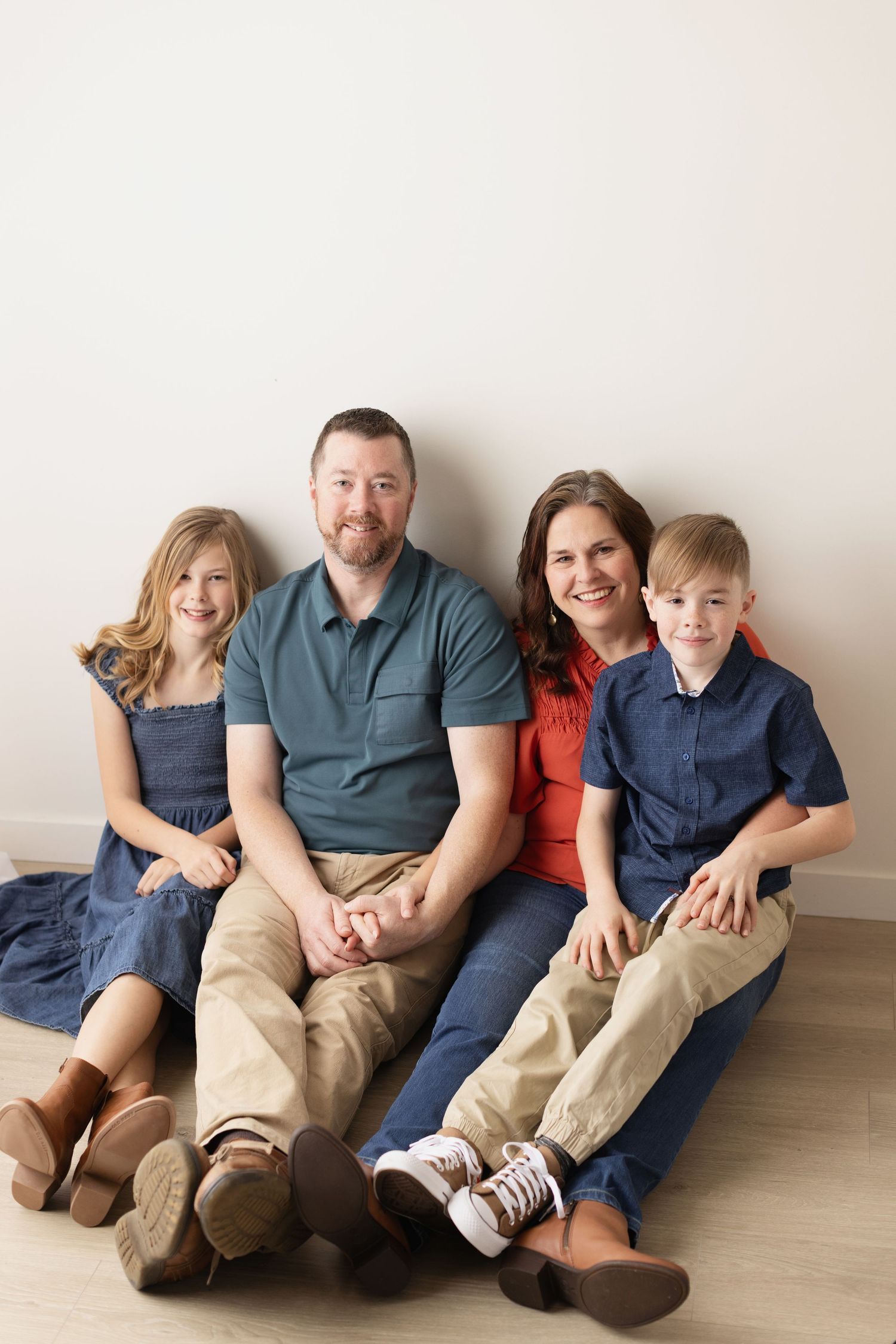 A family group lounges casually together on a light wood floor wearing coordinated navy and teal outfits. Elizabeth Lang Photography Surrey