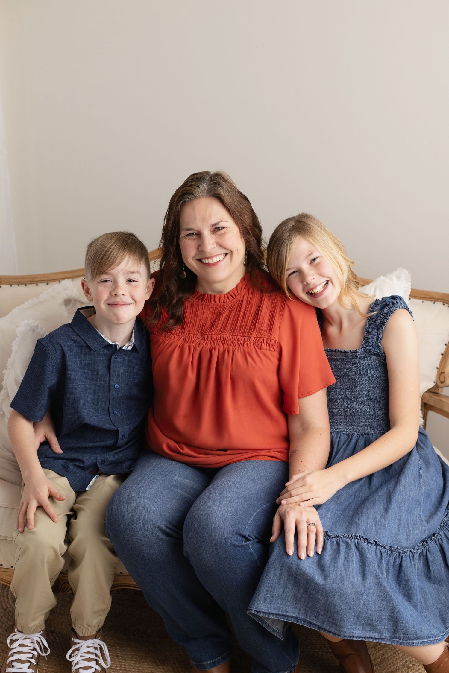 Three people wearing coordinated navy and rust colored outfits sit together on a cream colored couch. Elizabeth Lang Photography Surrey