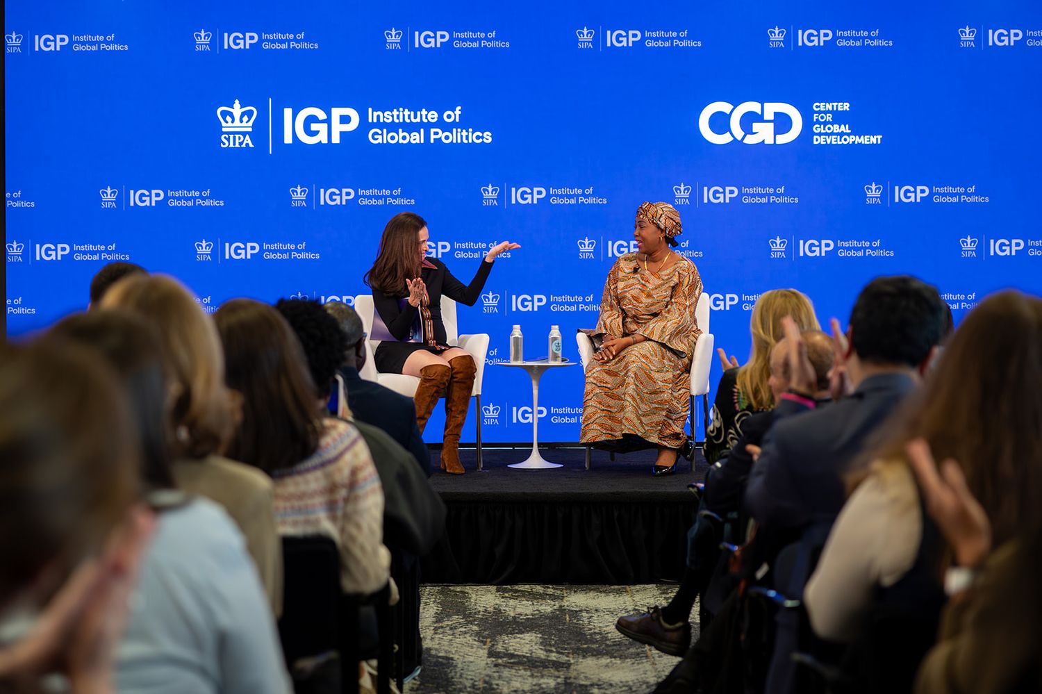 Conference panel discussion with speakers seated at a long table on stage with blue backdrop and IGP branding.