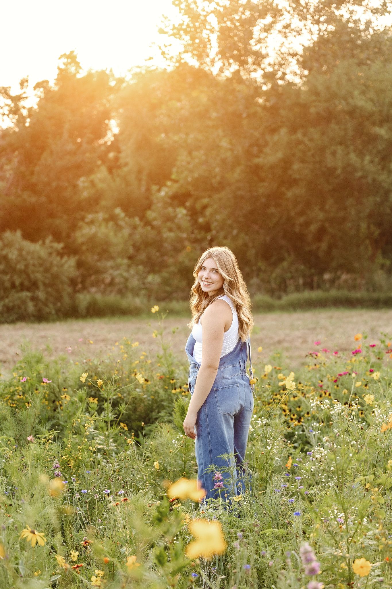 A person in a blue dress stands in a wildflower meadow at golden hour with sunlight filtering through trees.