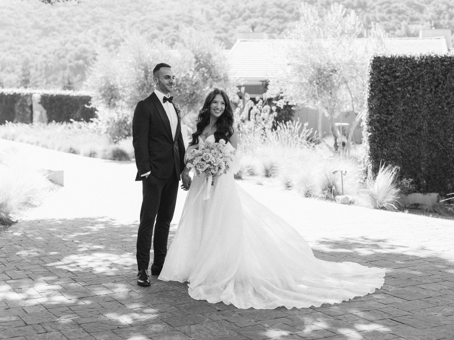 Black and white photo of wedding party laughing together under a tree during an outdoor celebration.