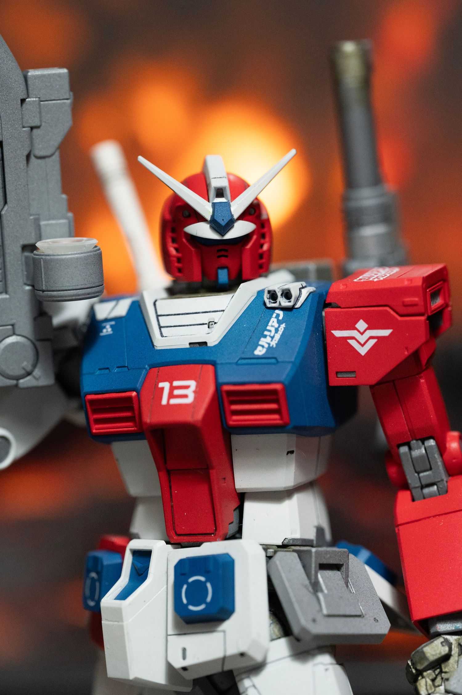 Close-up shots of a red and blue Gundam model figure head against an orange background with dramatic lighting.