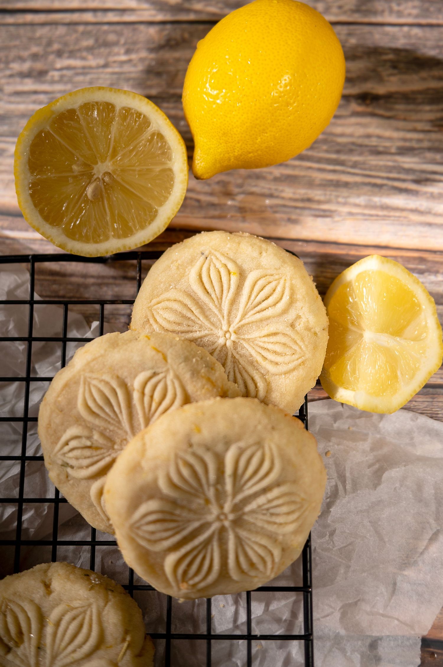 Fresh lemons and butter cookies with floral designs cooling on a wire rack against rustic wooden background.