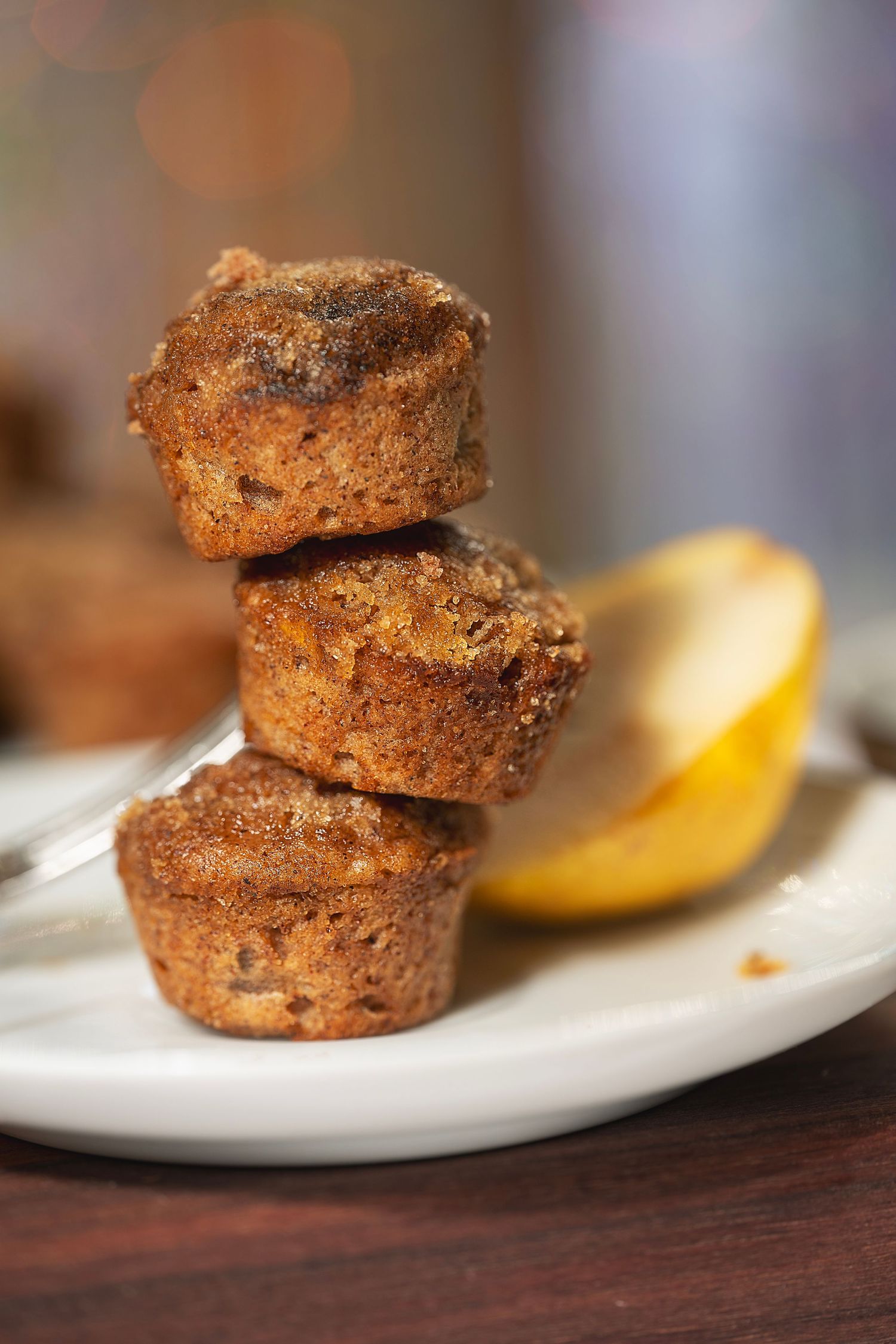 Three stacked homemade muffins with a golden brown crust served on a white plate next to a lemon slice.