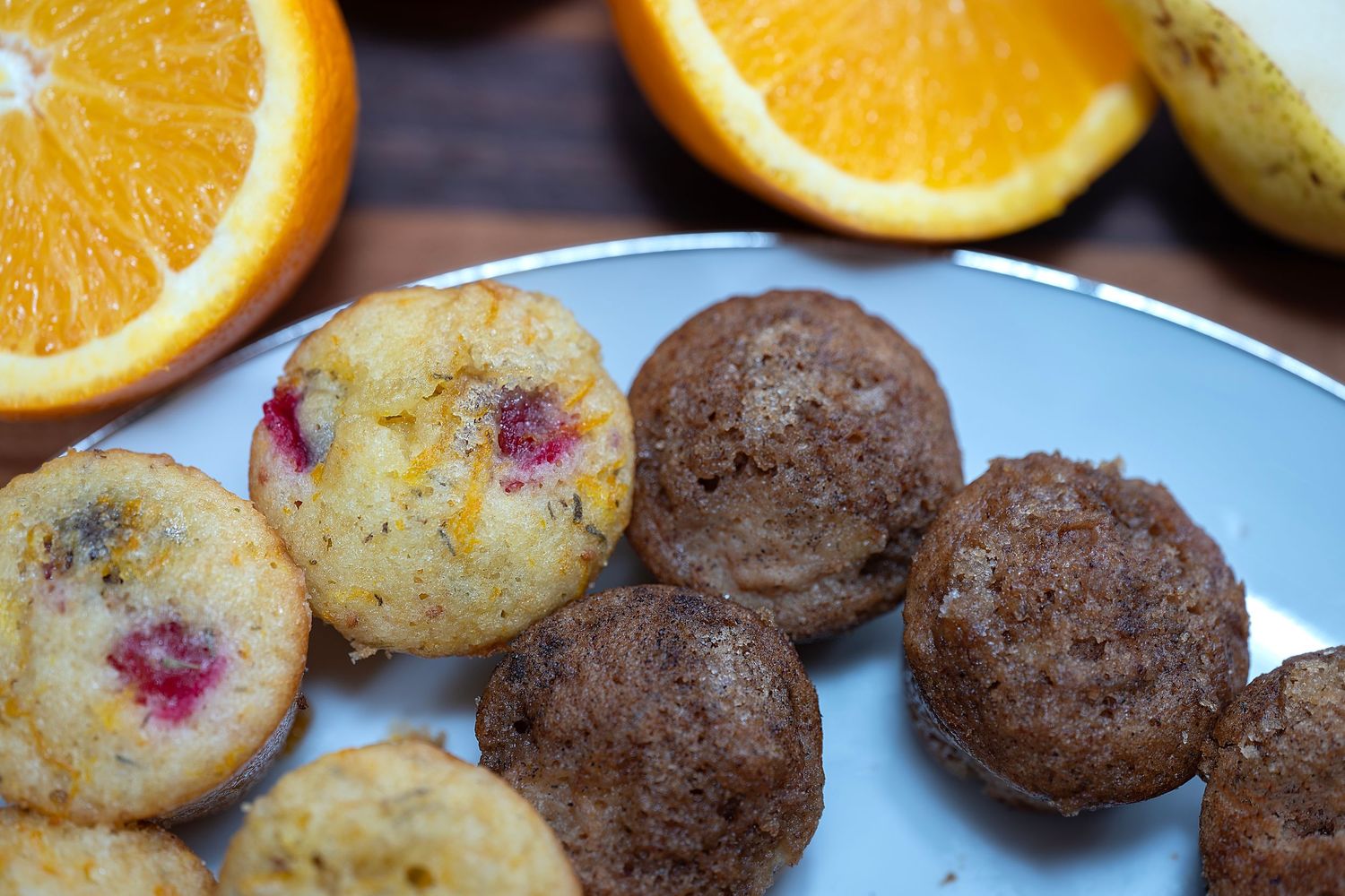 Homemade orange cranberry muffins displayed alongside chocolate cookies on a blue and white plate.
