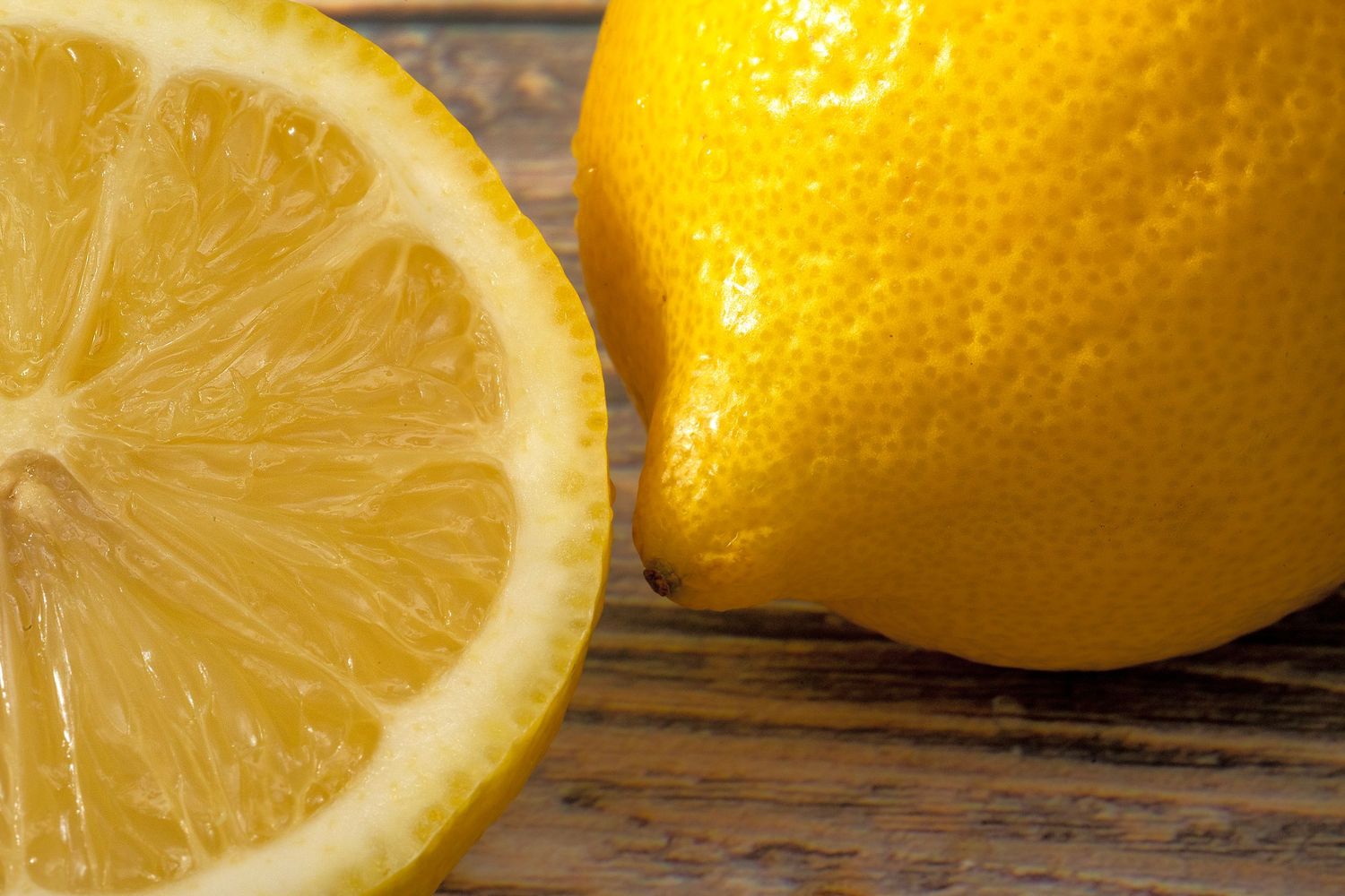 Fresh yellow lemons and cut lemon slices arranged on rustic wooden background.