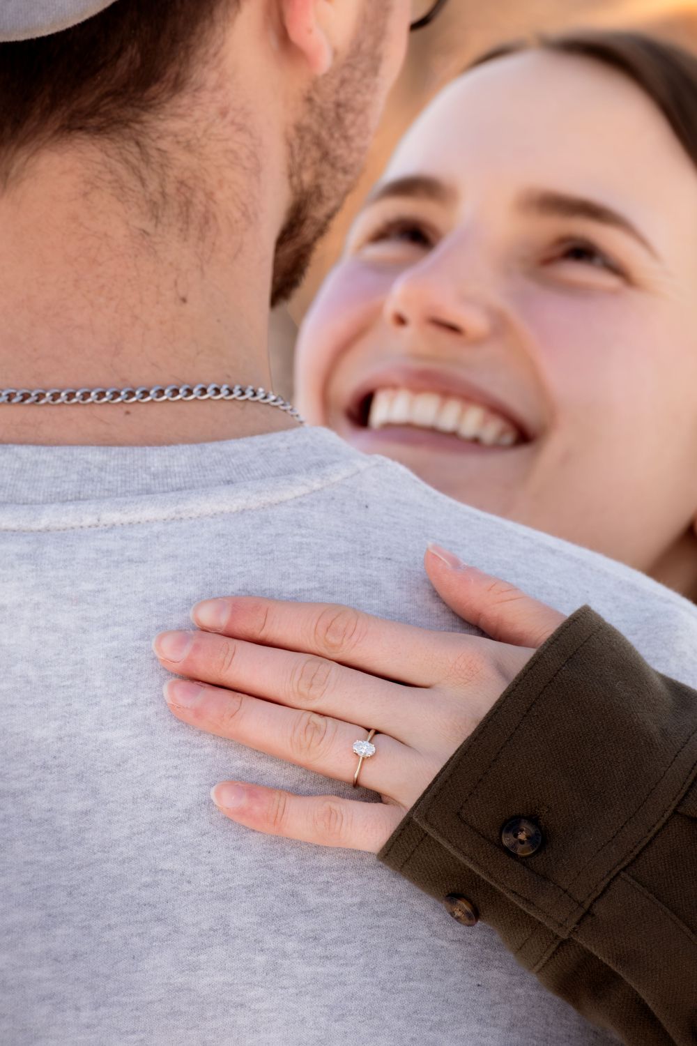 Couple wearing casual clothing embracing while showing their wedding rings in warm sunlight.