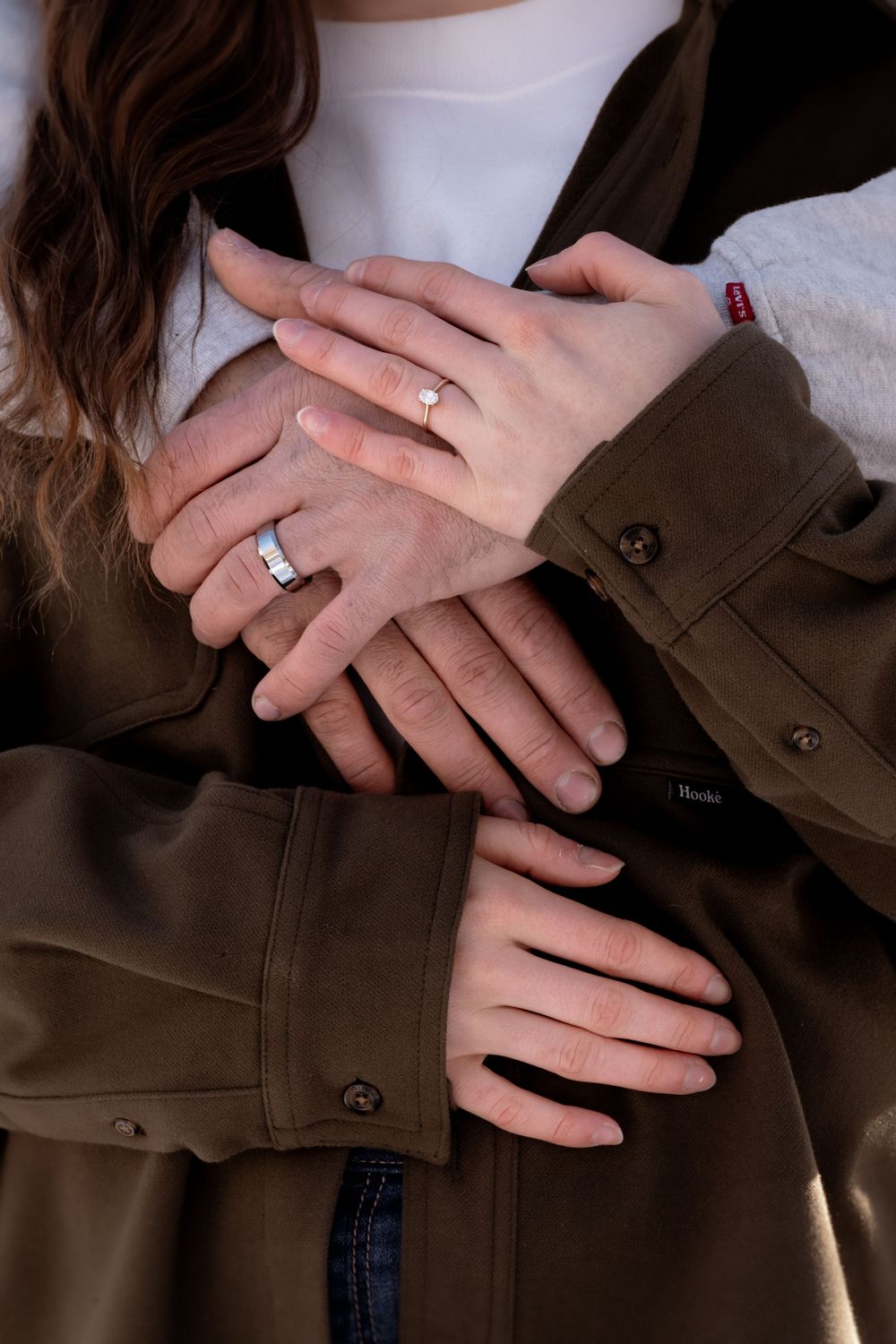 Couple's hands intertwined showing wedding rings and brown jacket sleeve in intimate gesture.