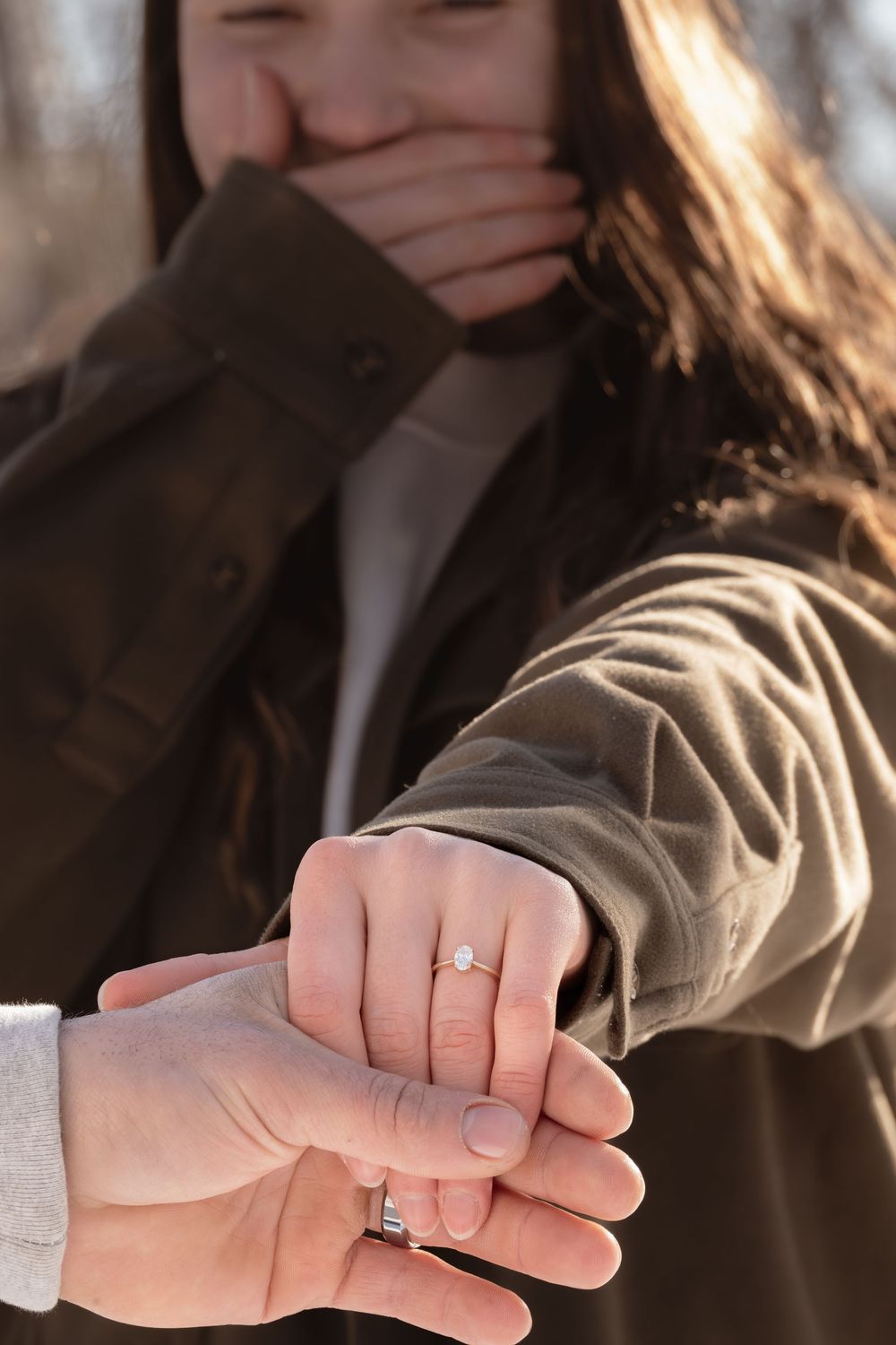 Close-up shot of hands showing off engagement rings while someone covers their smile in background.
