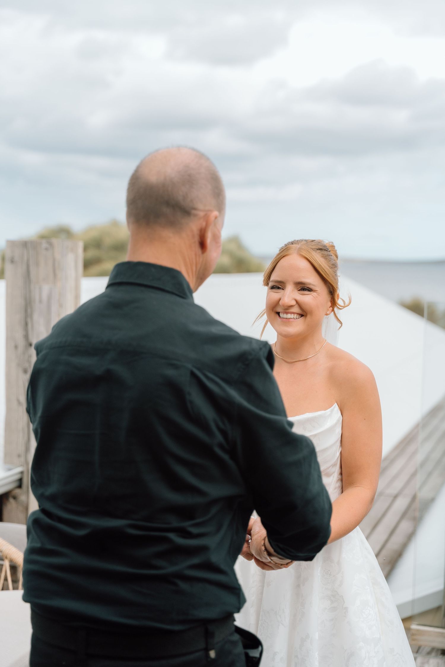 A series of candid moments between a bride in white and someone in black on a wooden dock by the water.