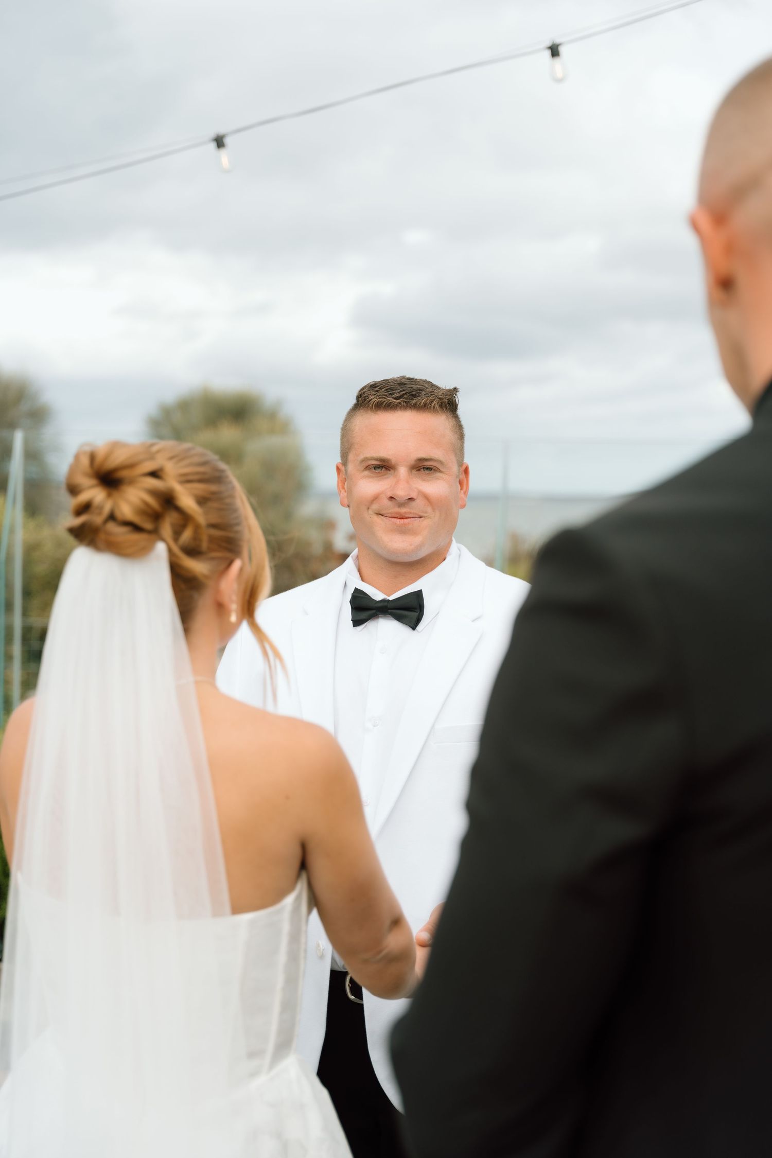 A wedding ceremony moment captured outdoors with the bride and groom in formal attire under cloudy skies.