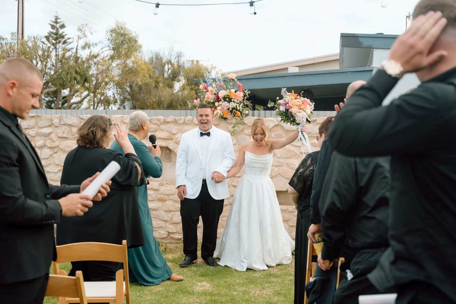 Wedding guests mingle at an outdoor reception with string lights overhead.
