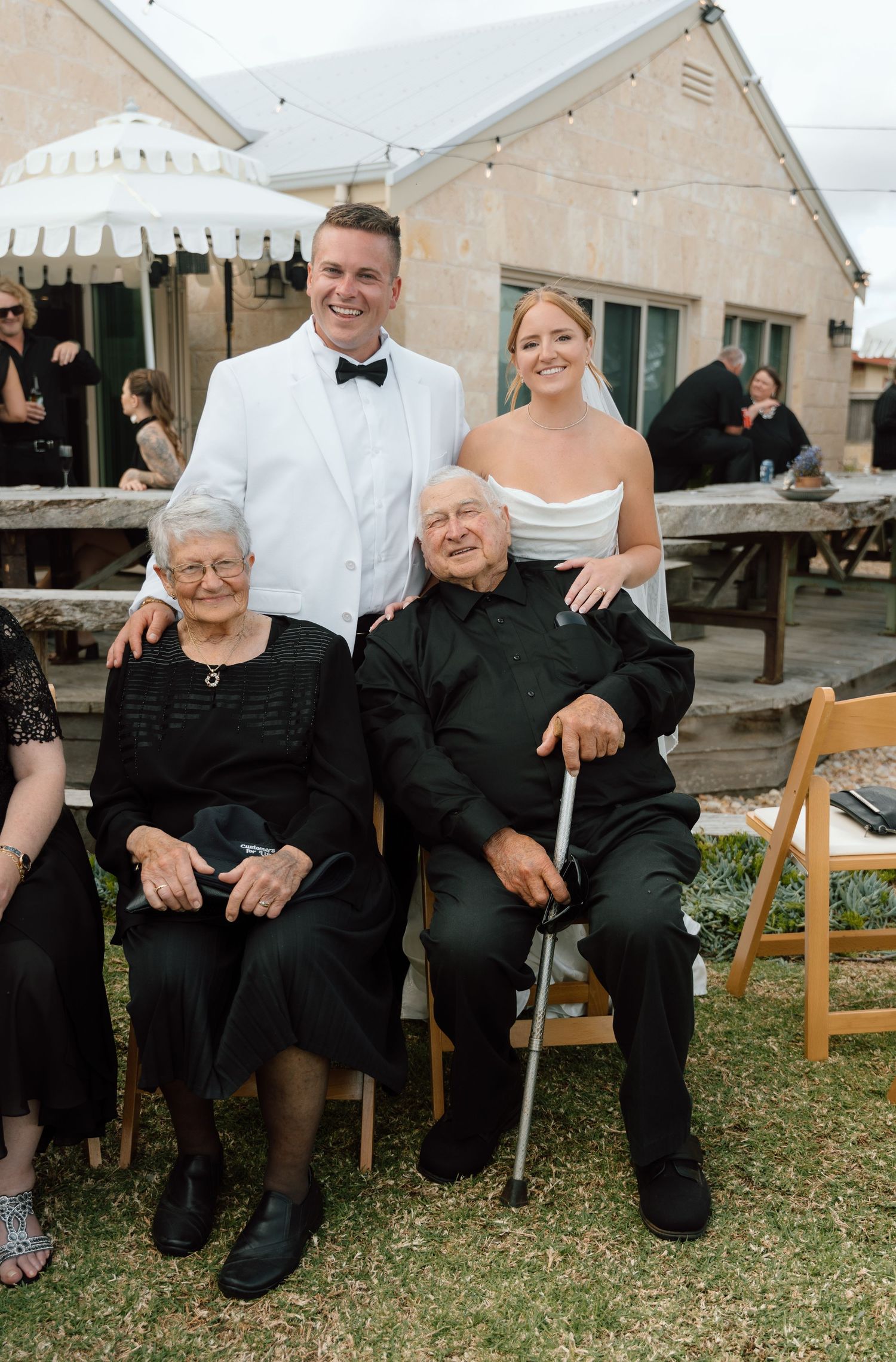 Wedding guests seated on wooden chairs at an outdoor reception venue.