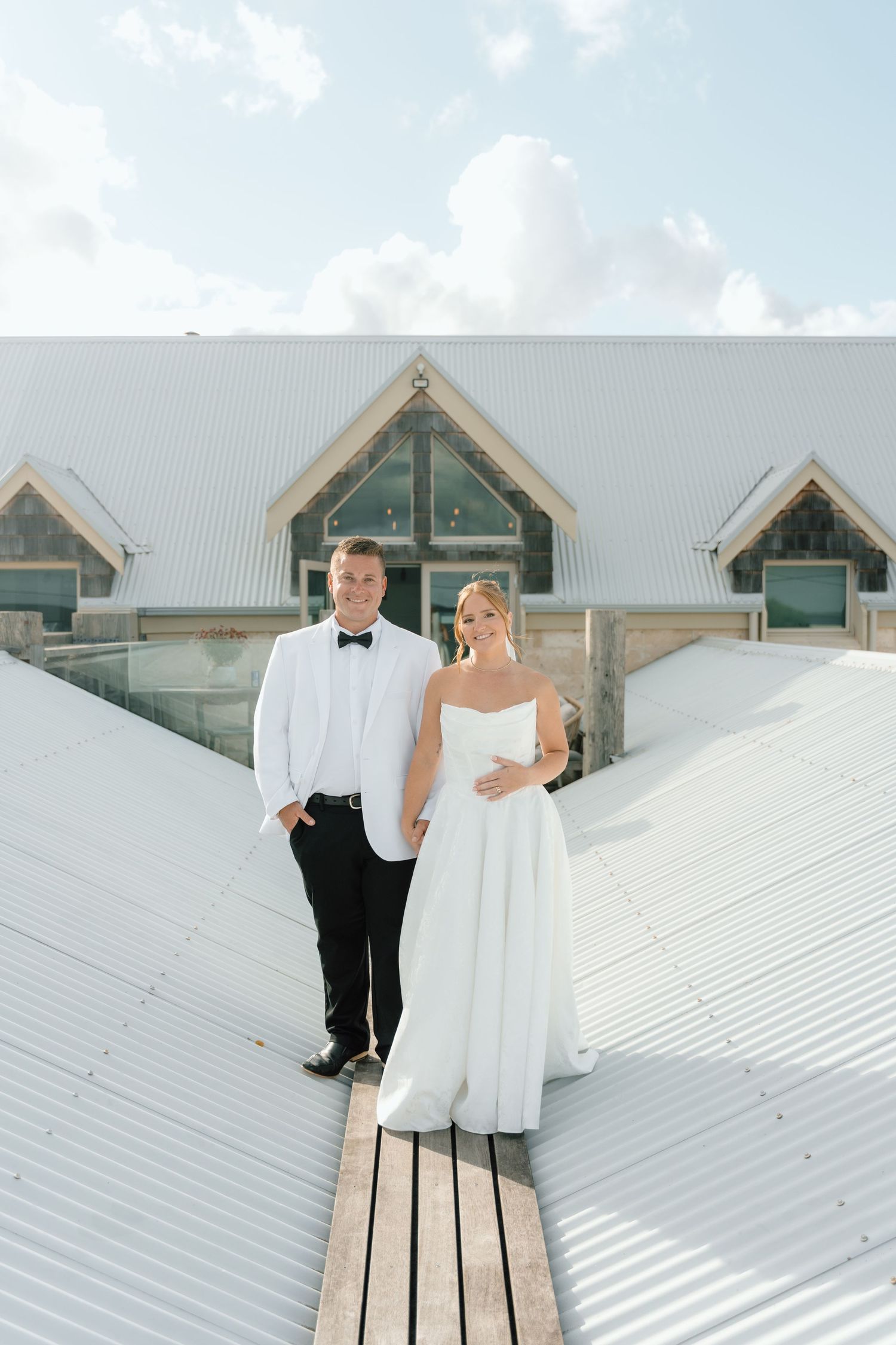 A couple poses on a white metal roof with rustic buildings in the background.