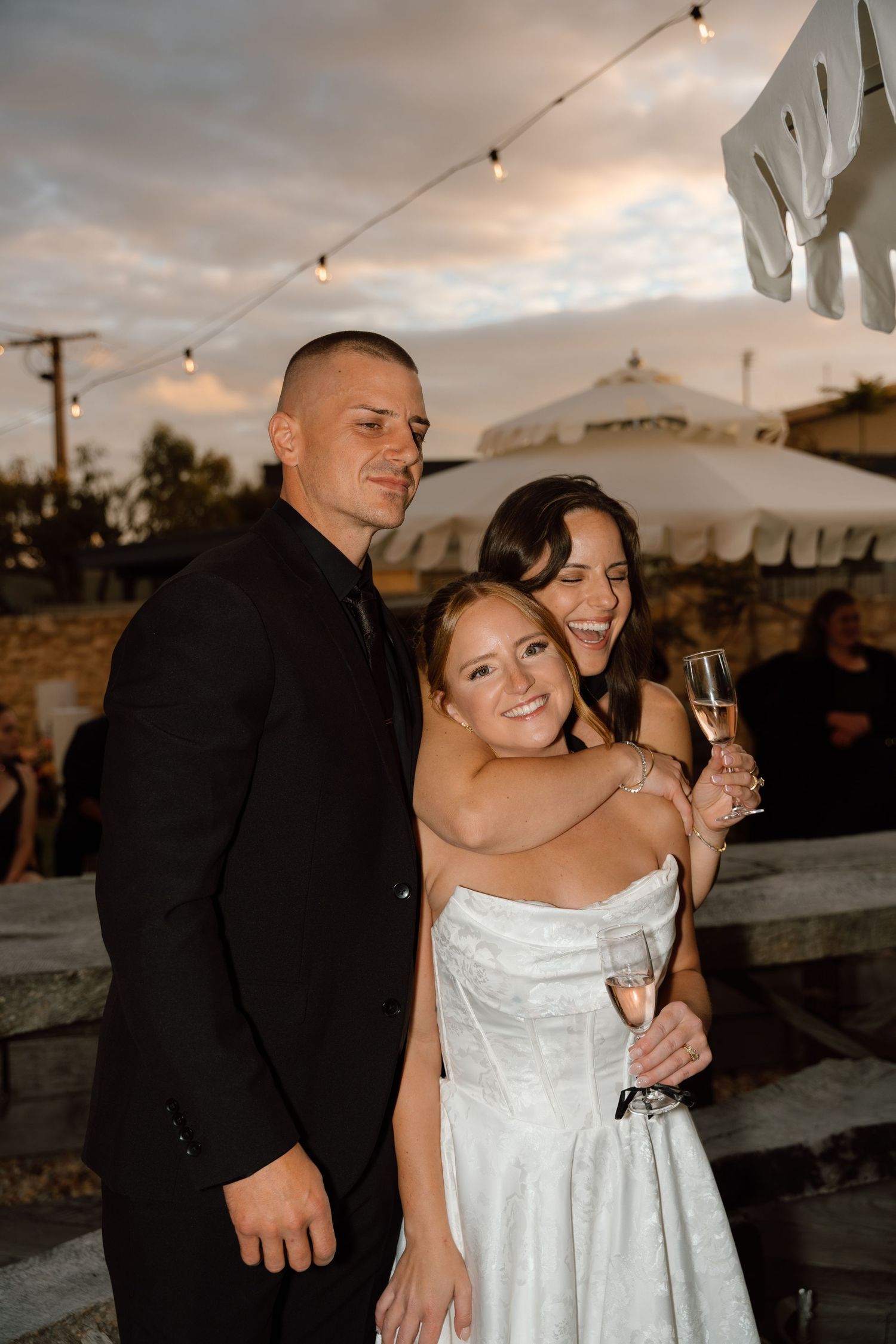 Wedding guests celebrate under string lights at sunset during outdoor reception.