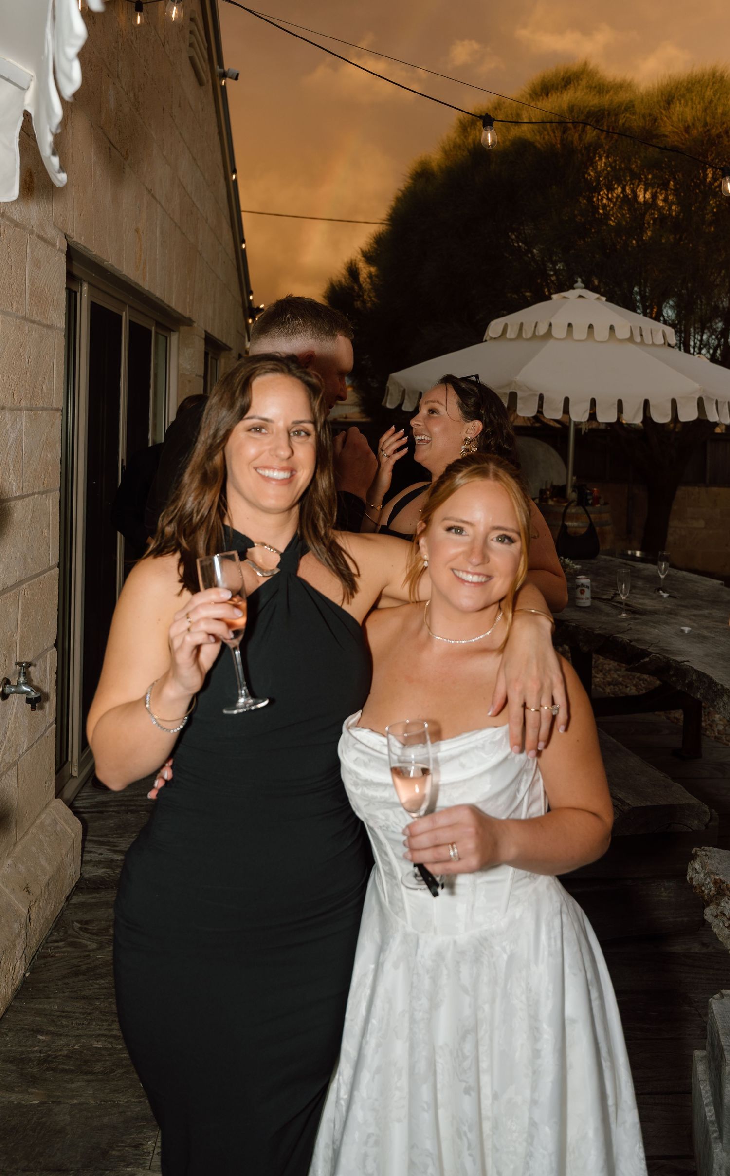 Wedding guests in formal attire celebrate during sunset at an outdoor reception.