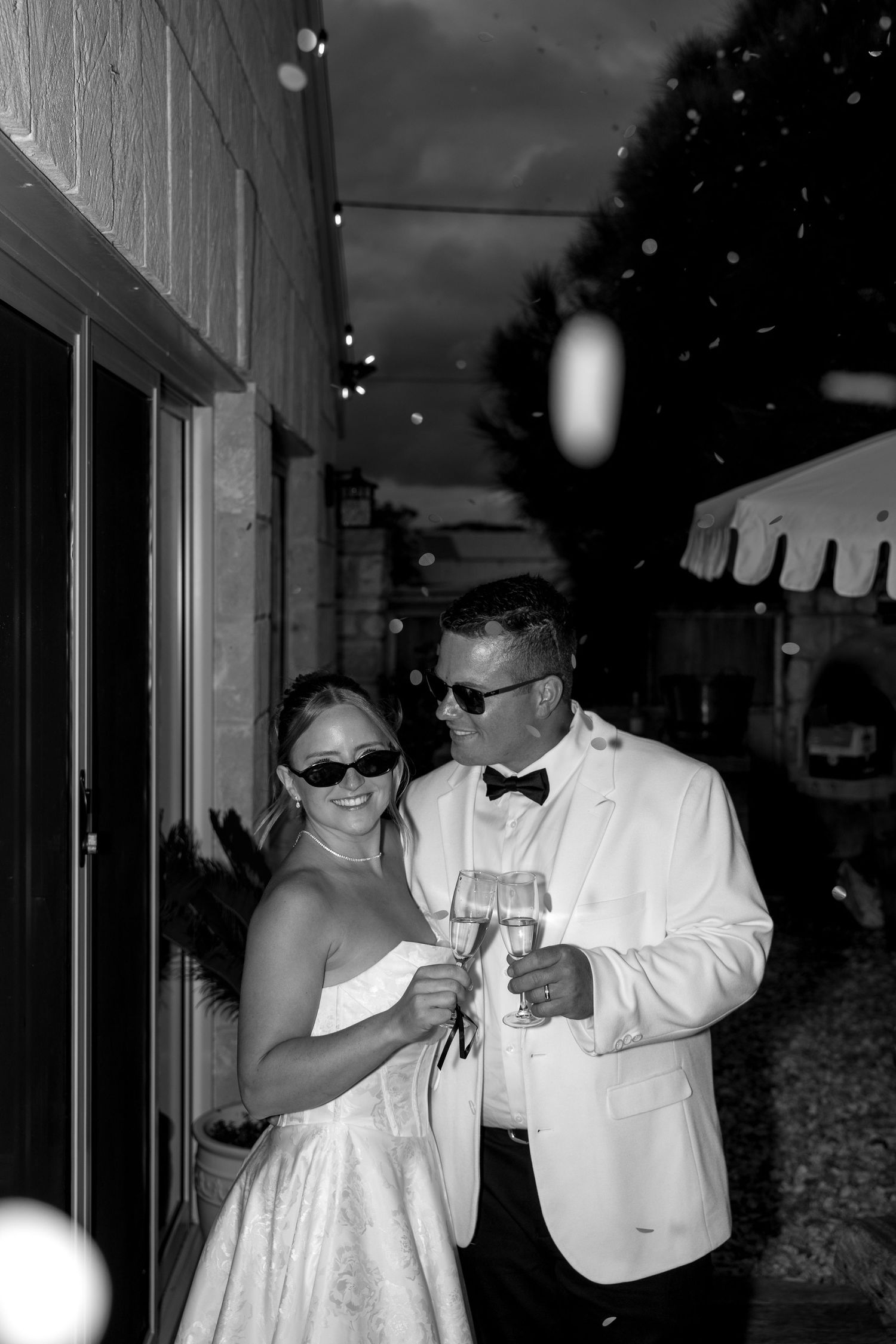 Wedding party members in formal wear pose with sunglasses at dusk.