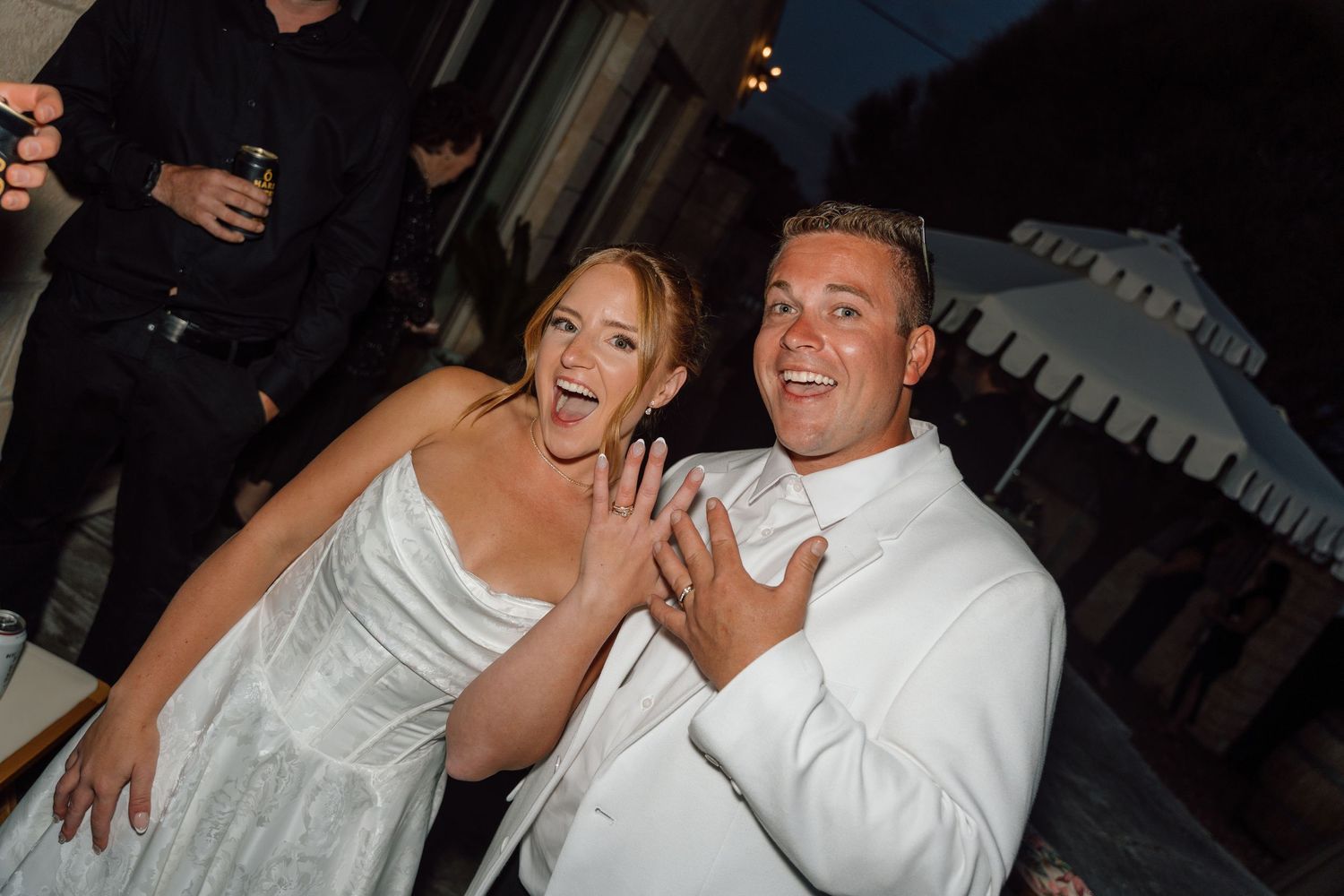 Two people in wedding attire laugh together joyfully during a celebration at night.