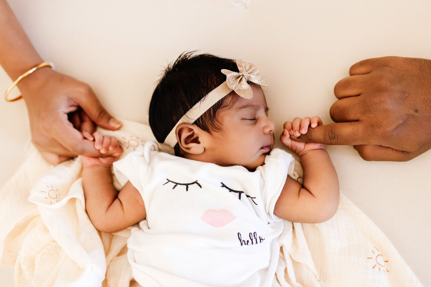 A newborn baby sleeps while holding her parents' fingers at her in-home newborn session