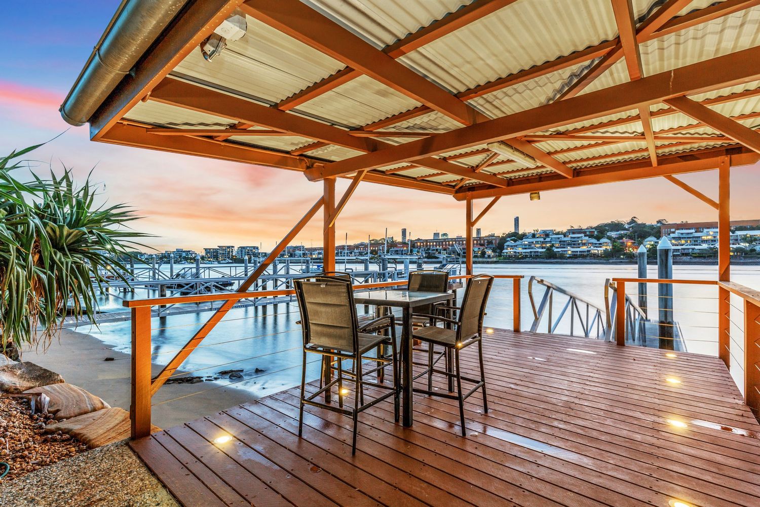 Covered timber deck with dining set overlooking scenic waterfront at sunset.