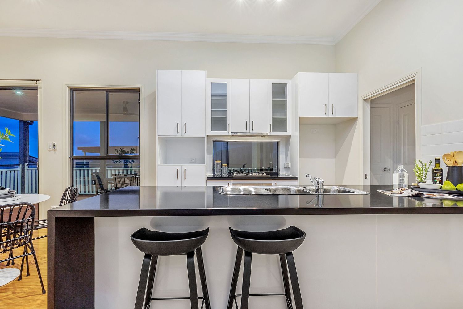 Modern white kitchen with dark stone island bench and bar stools.
