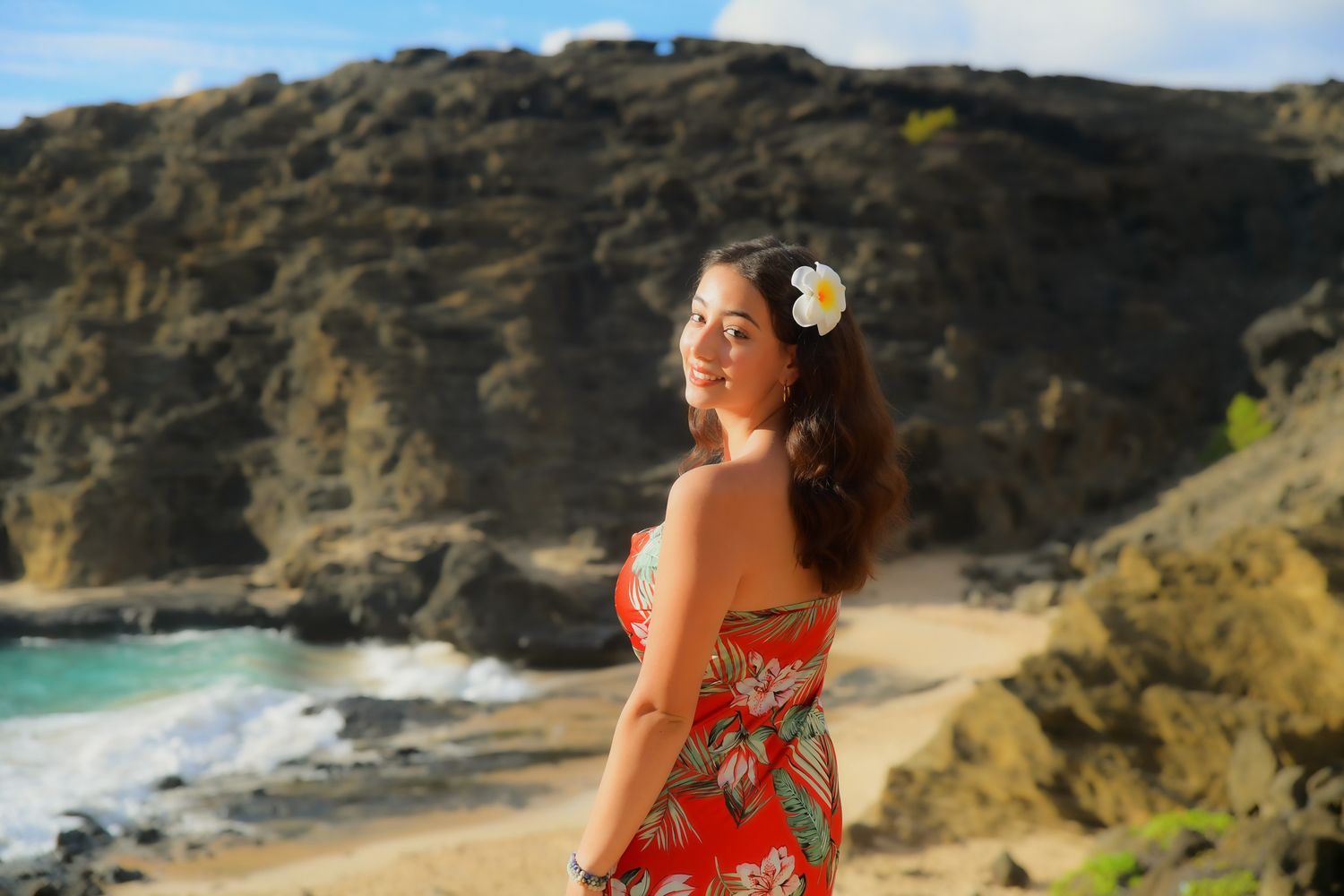 Woman in floral dress enjoying scenic coastal views along rocky cliffs and turquoise waters in Hawaii.
