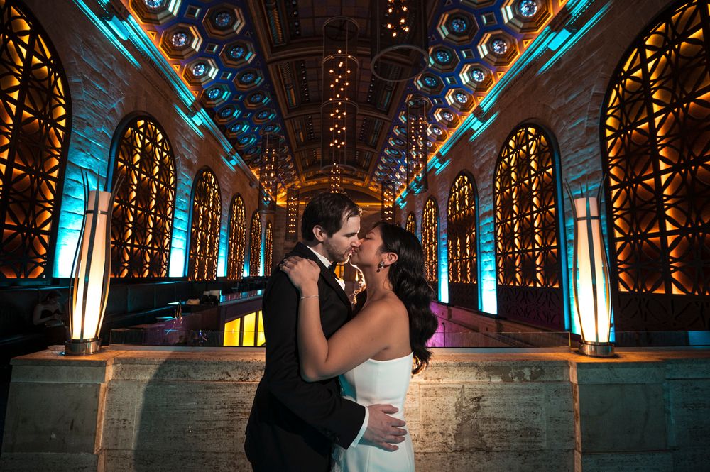 Wedding couple dances in an elegant ballroom with turquoise uplighting and ornate gold decor.