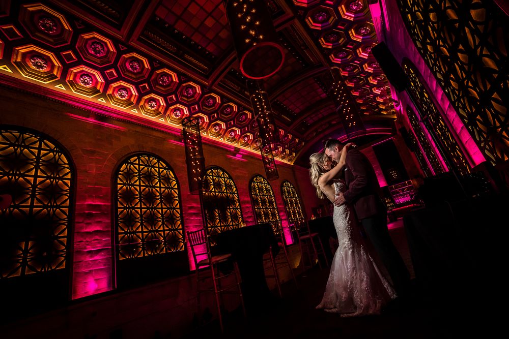 Wedding couple dancing under ornate arched ceiling with magenta uplighting creating a romantic atmosphere.