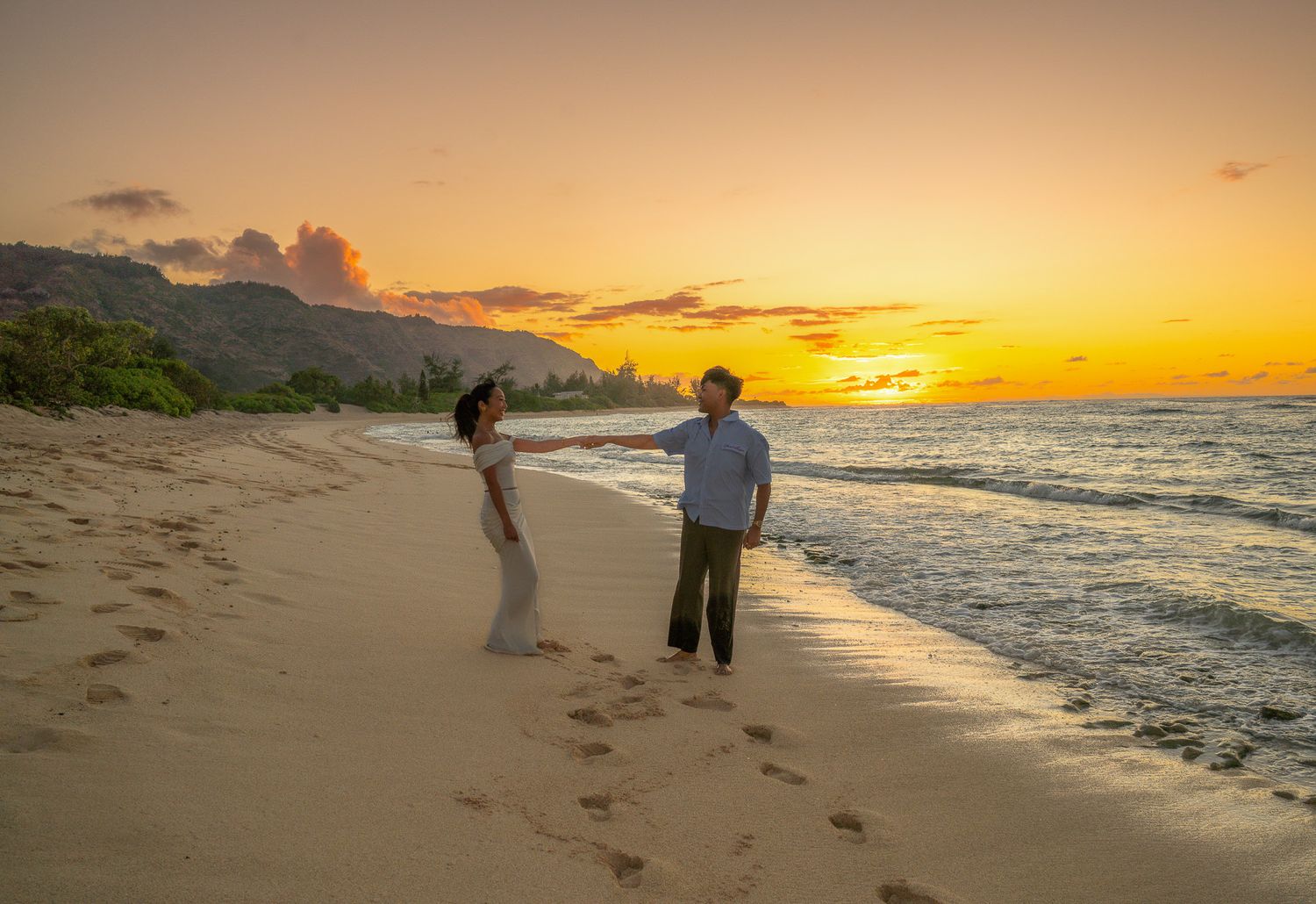Couple walking along a scenic beach at sunset with golden light reflecting off the ocean waves.