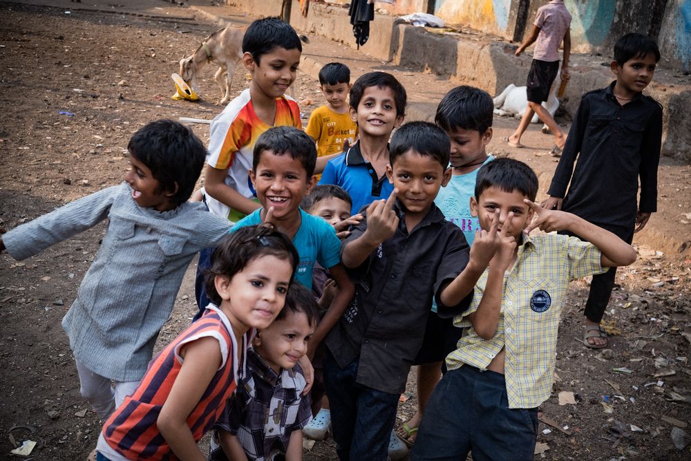A large group of smiling Indian children gathered together outdoors, waving and posing for the camera.