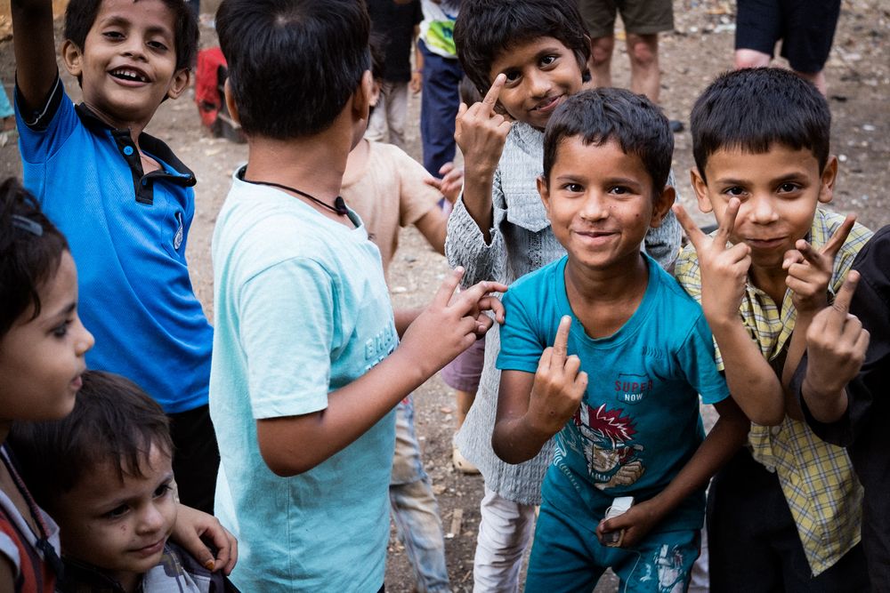 Group of smiling children posing and making peace signs in an urban neighborhood in India.