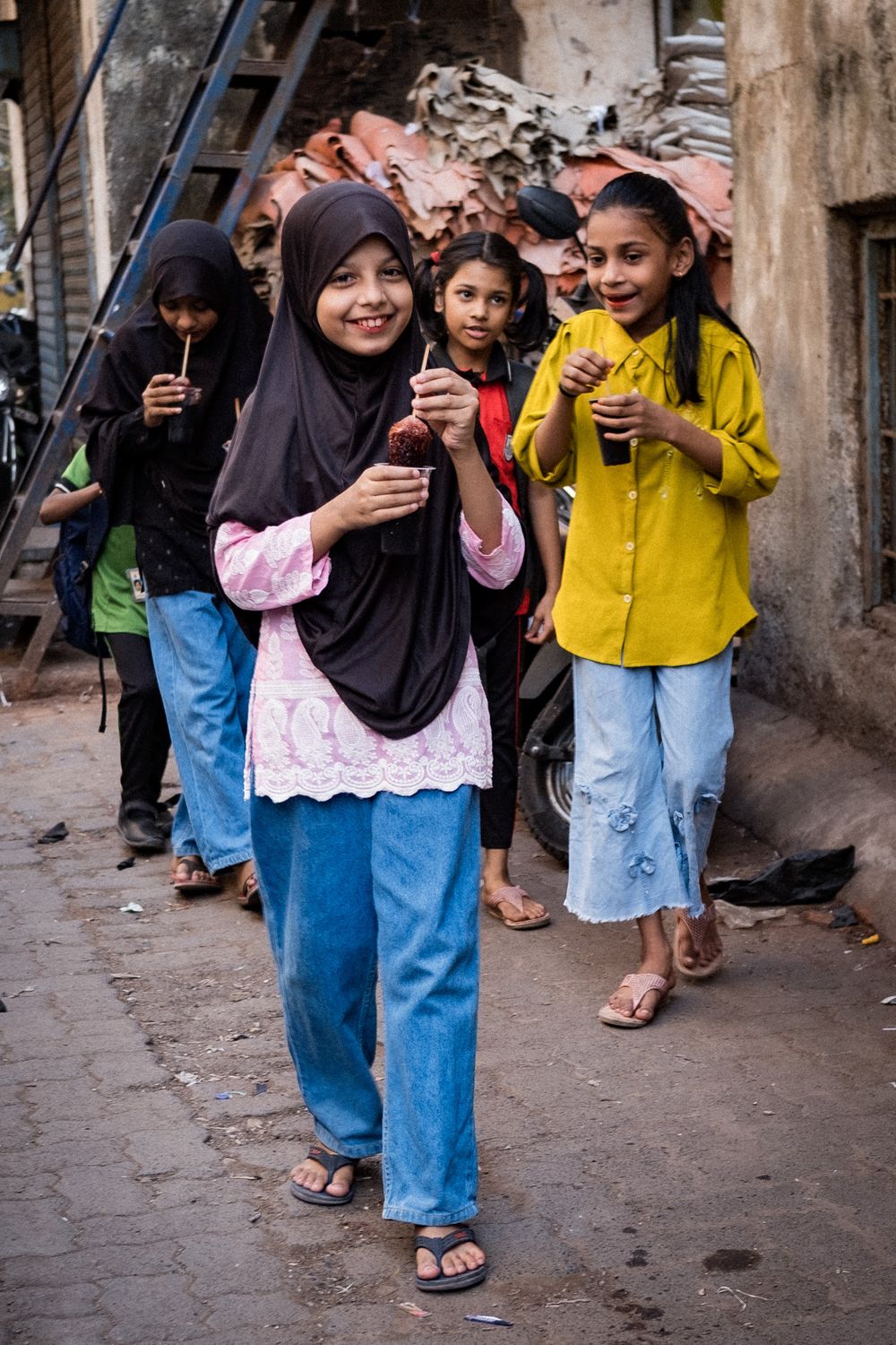 Young girls in colorful clothing enjoying street food snacks in a narrow alley in India.