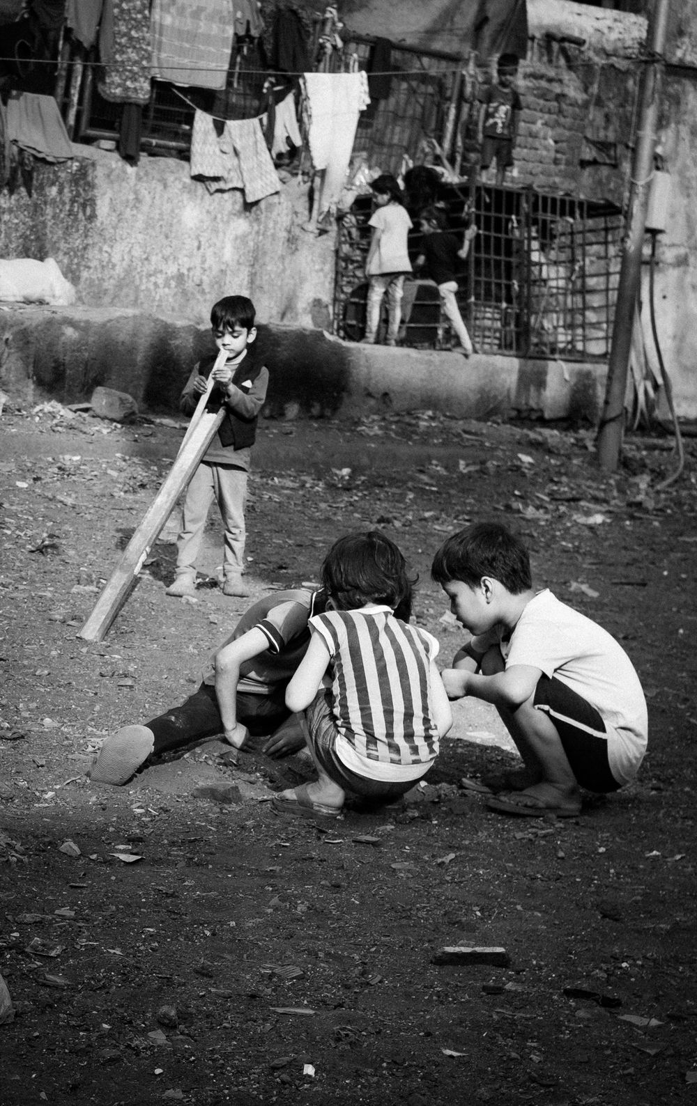 Black and white photo of children playing cricket in a poverty-stricken urban neighborhood.