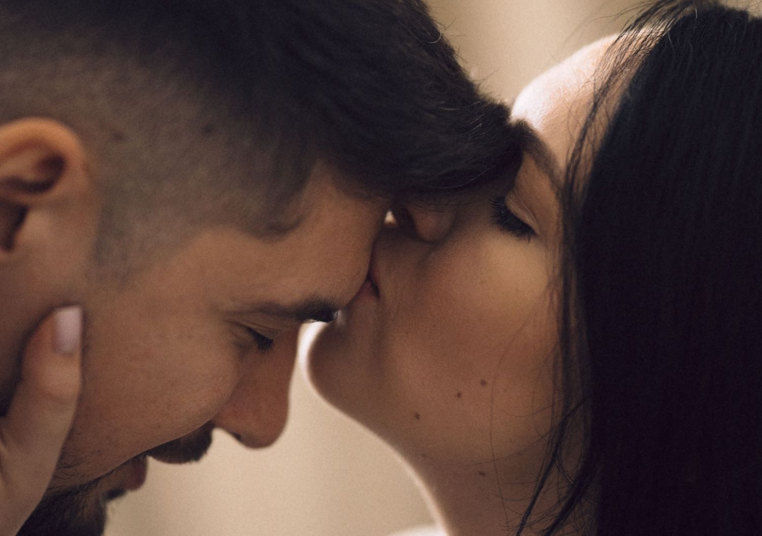 Two people share an intimate moment in a romantic close-up shot with warm lighting.