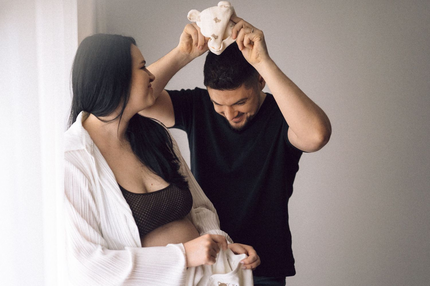 Intimate black and white maternity photo session showing couple in tender embrace against neutral background.