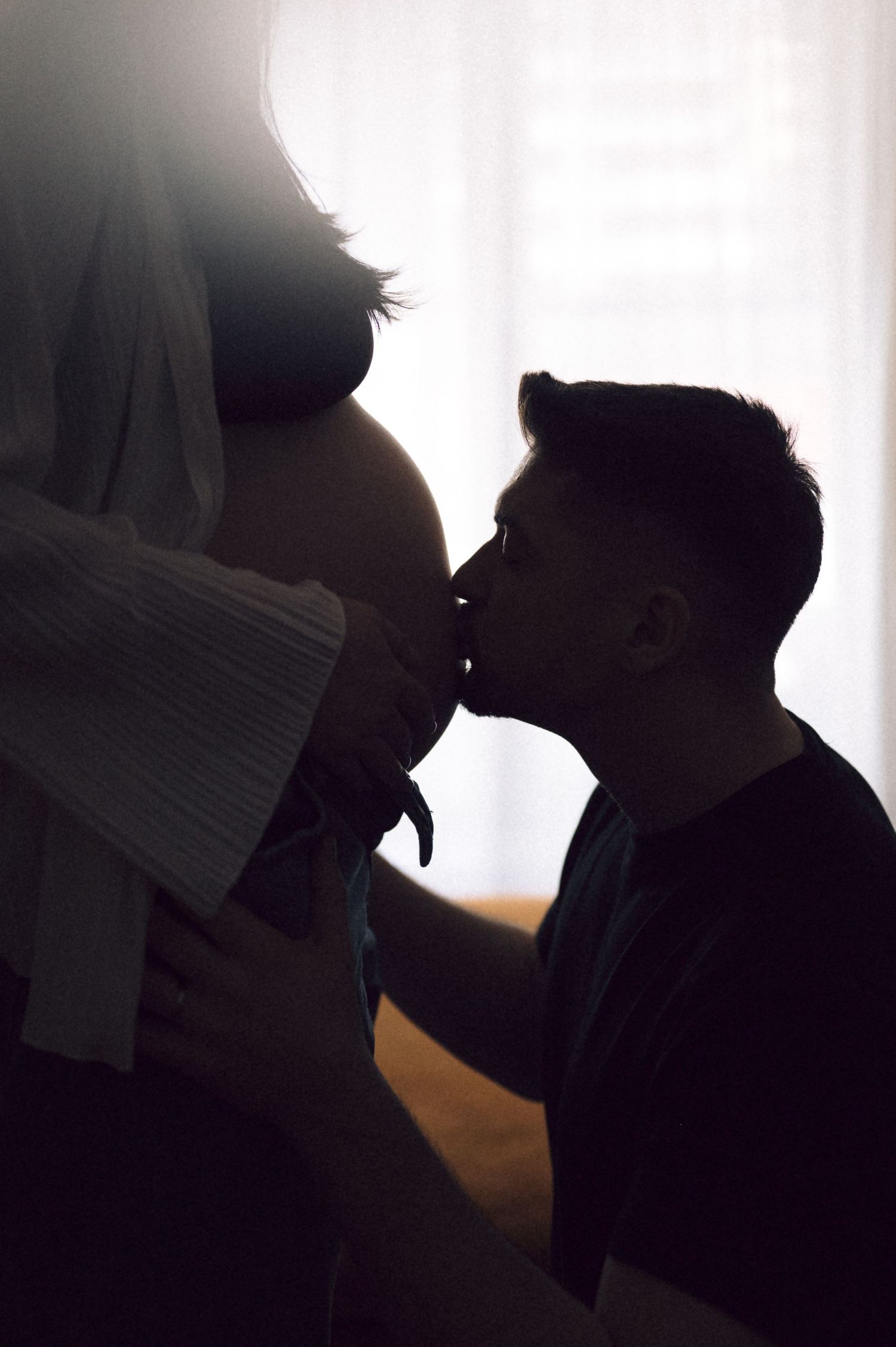 Silhouetted figures in an intimate moment against a bright window background.