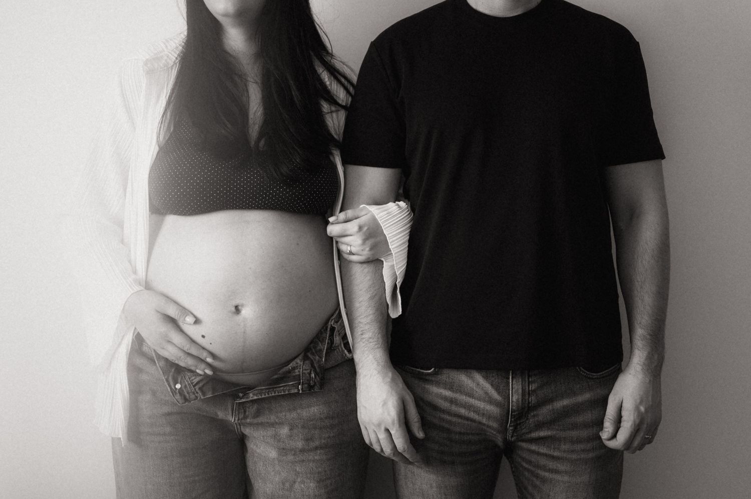 Black and white photo showing a pregnant woman's belly next to someone in a black t-shirt and jeans.
