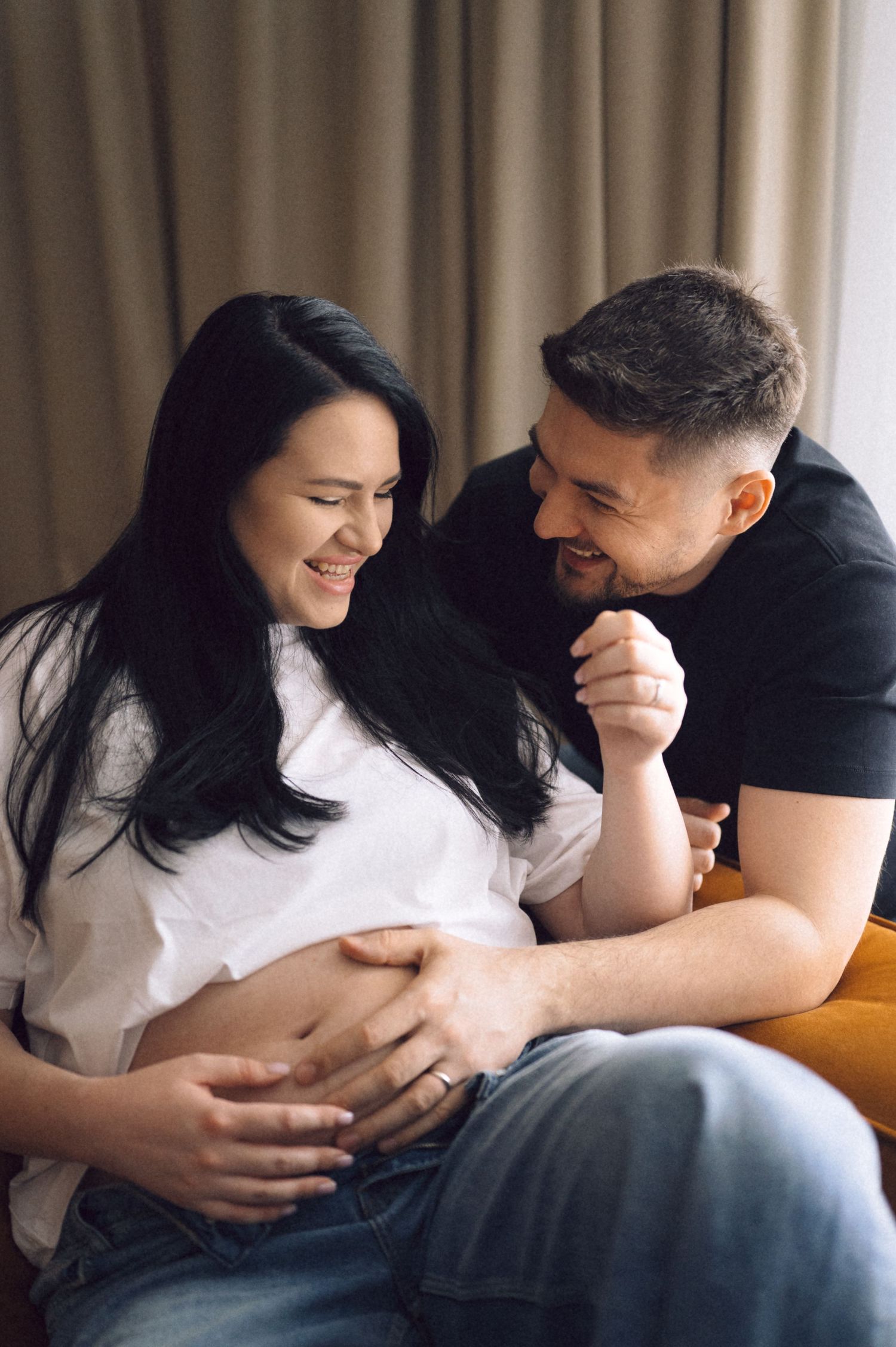 Candid pregnancy photoshoot showing couple sharing emotional moments on couch.