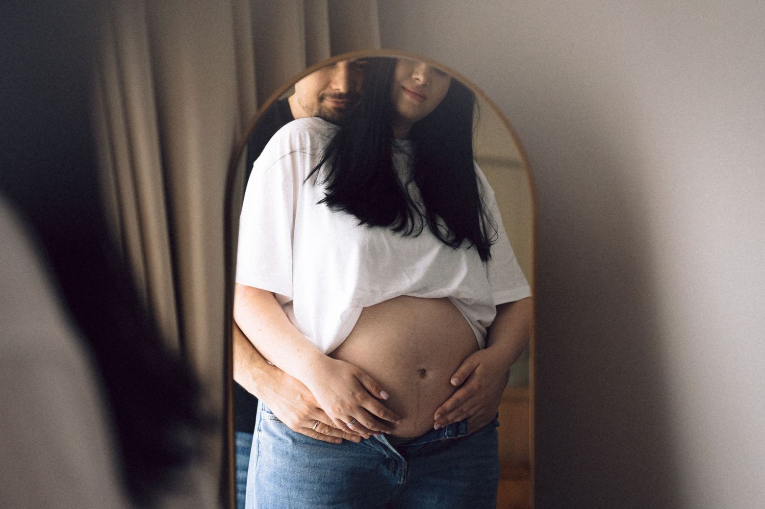 A series of photos showing a growing baby bump through different stages of pregnancy against a white shirt background.
