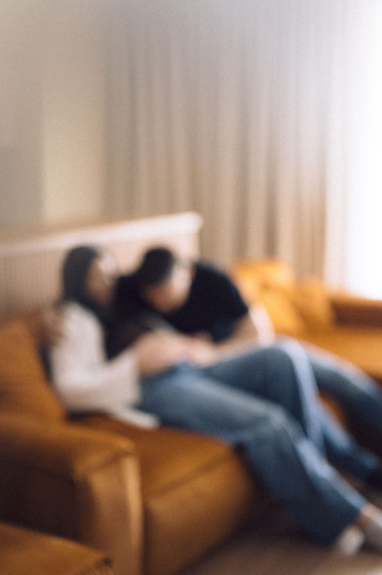 Blurred photo of someone resting on a brown leather couch in a softly lit room with curtains in the background.